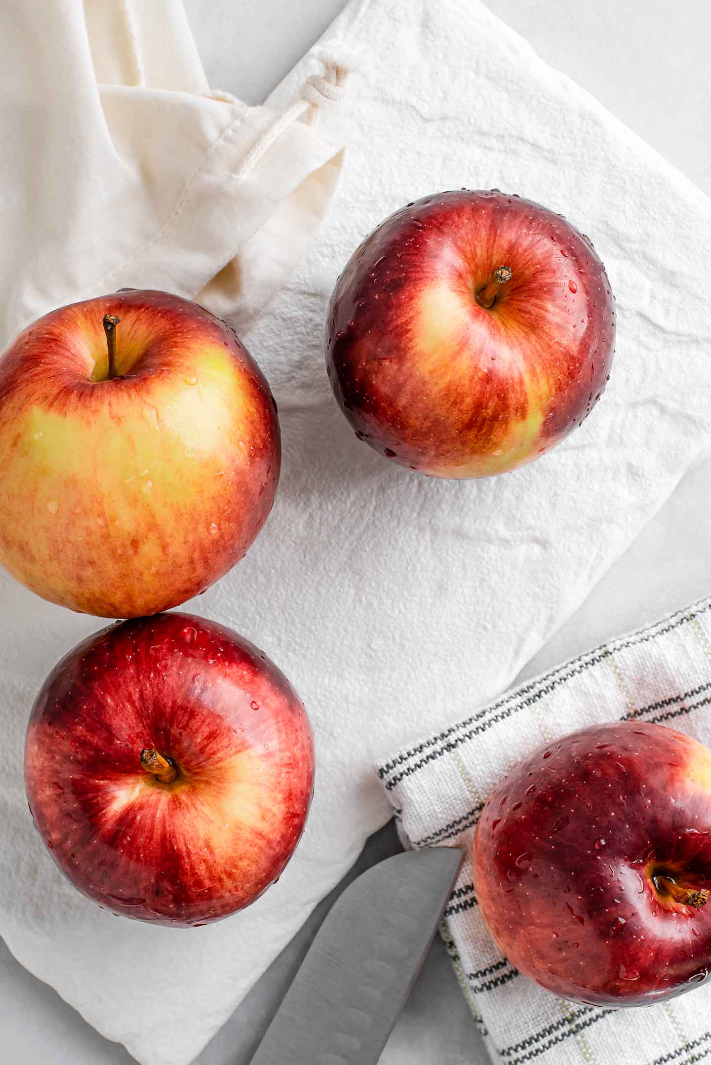 Top down view of four empire apples spilling out of a cloth bag onto a white tray.