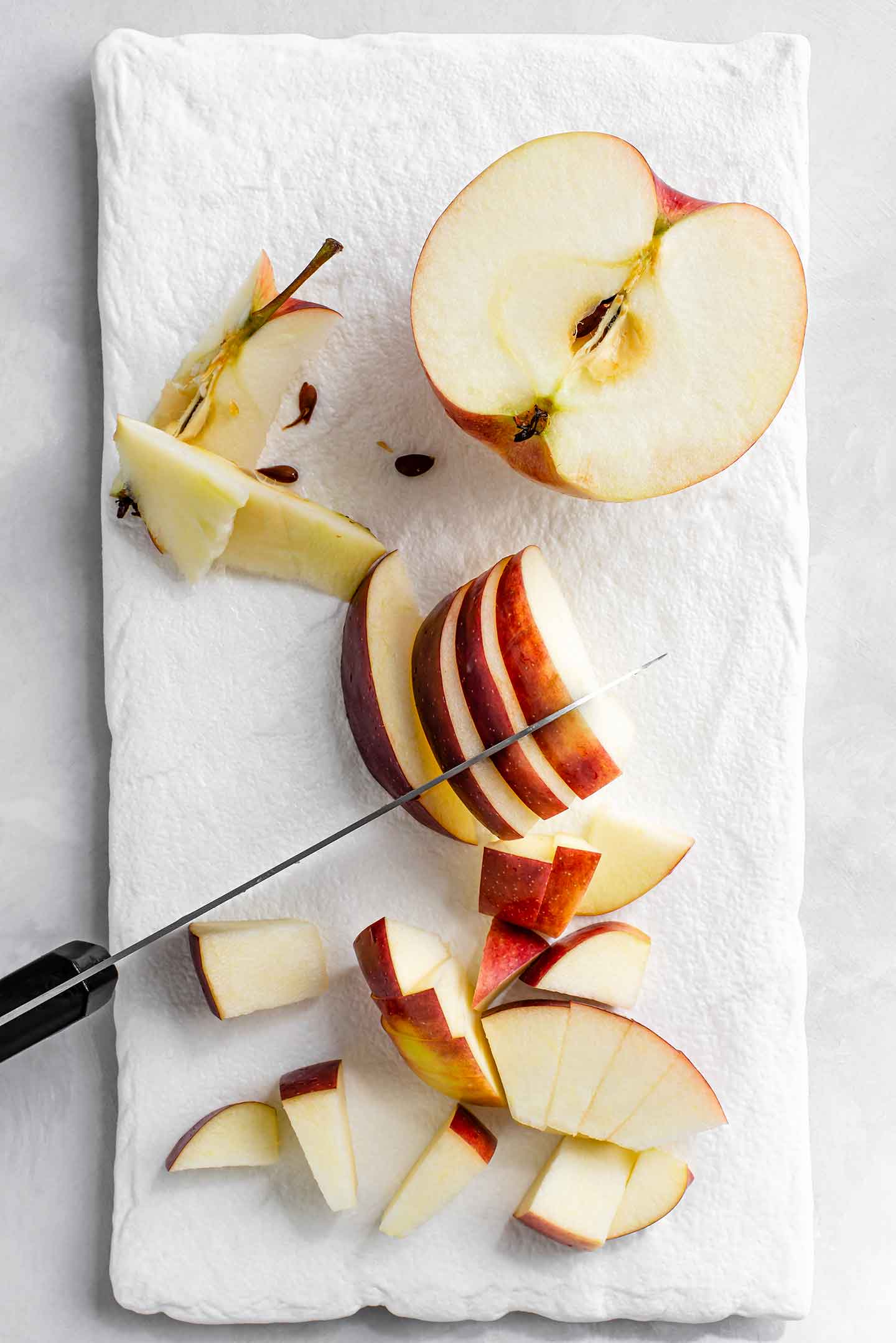Top down view of an empire apple being cored and diced on a white tray.