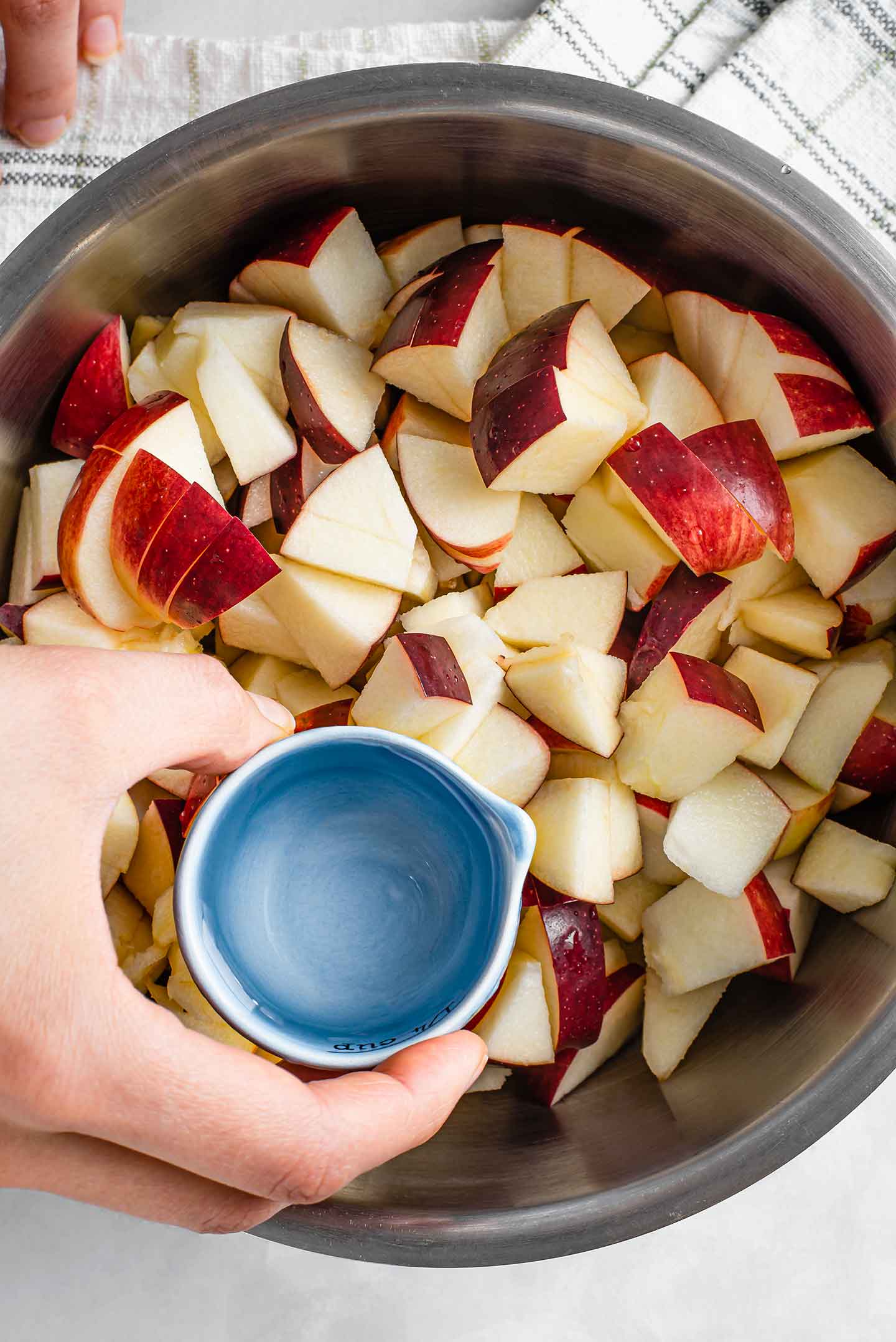 Top down view of diced apples in a saucepan with a small amount of water being poured over top.