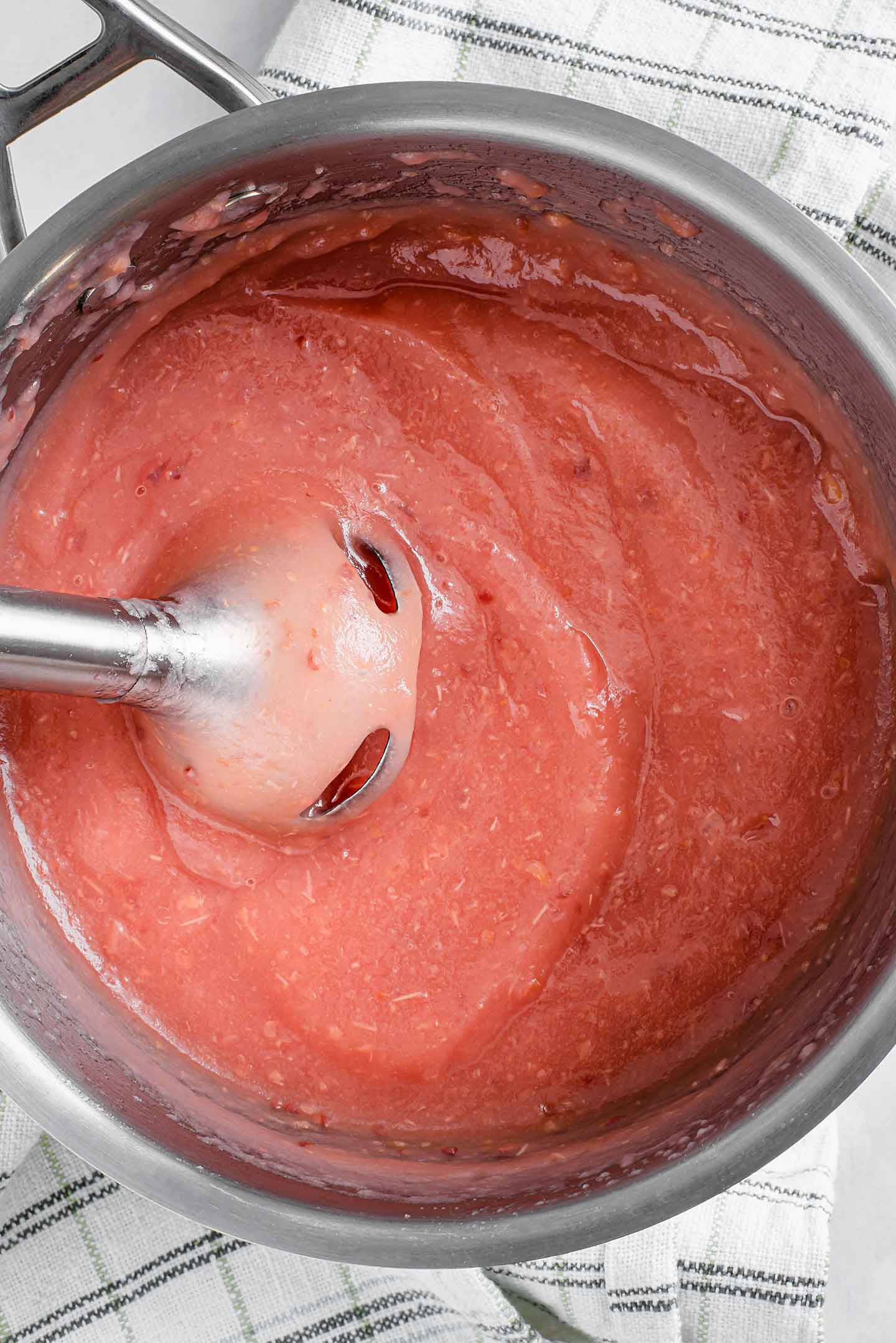 Top down view of pink applesauce being pureed with an immersion blender.