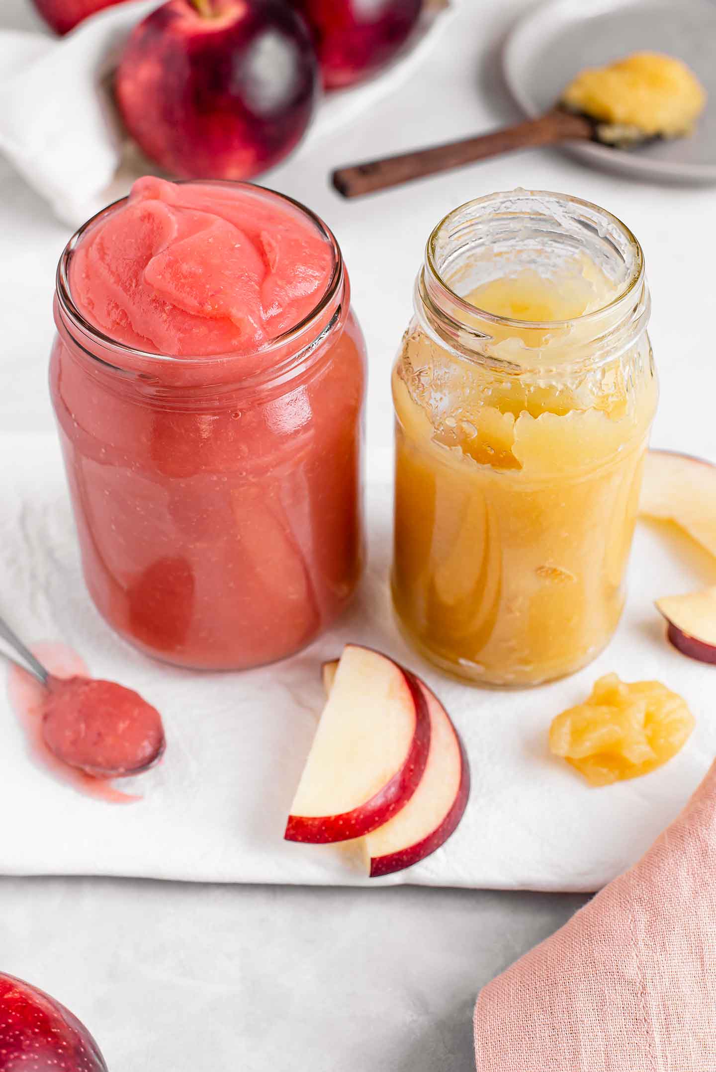 Side view of two glass jars with homemade applesauce. One is bright pink, the other is a golden coloured sauce.
