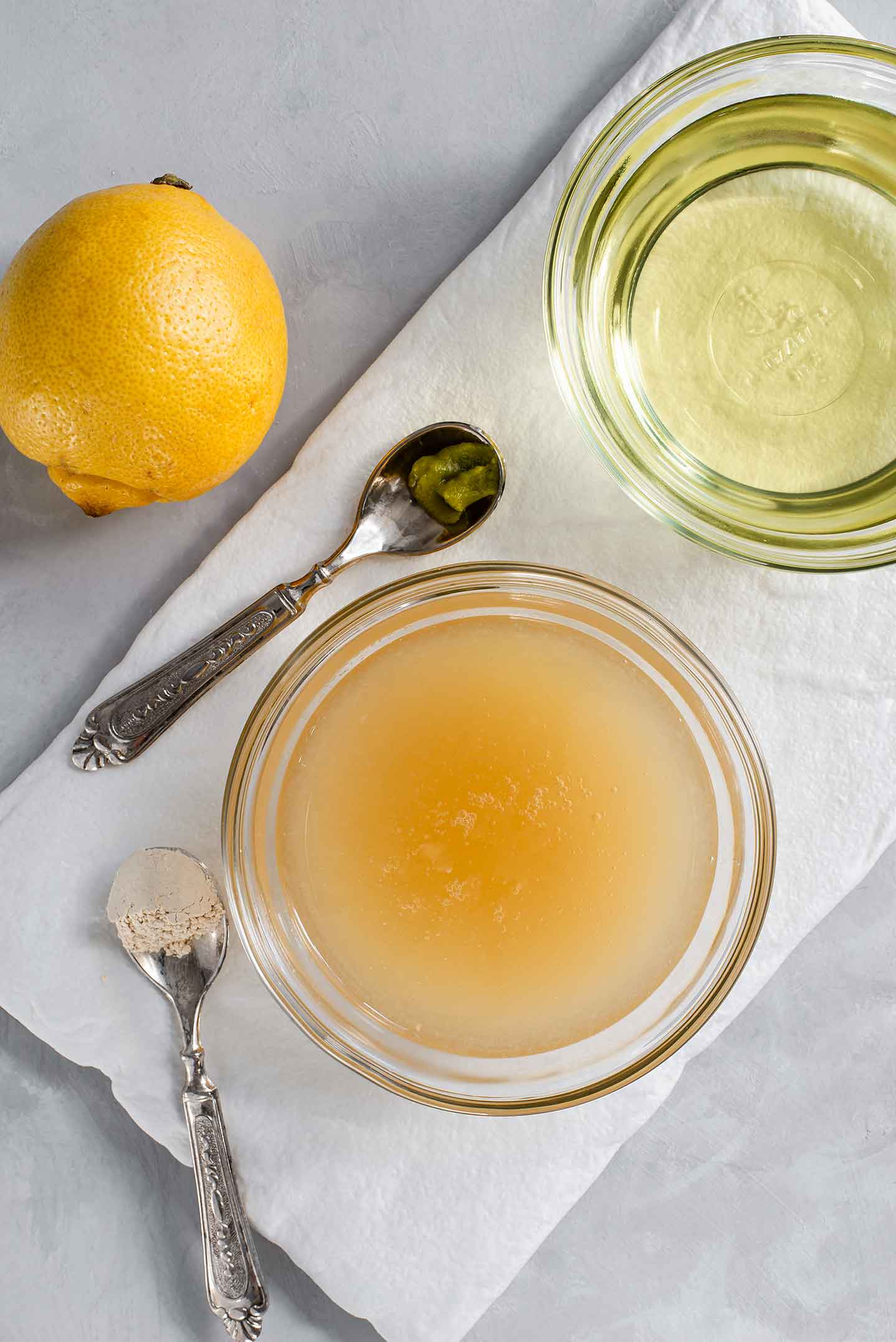 Top down view of aquafaba, canola oil, lemon, garlic powder, and wasabi on a white tray.