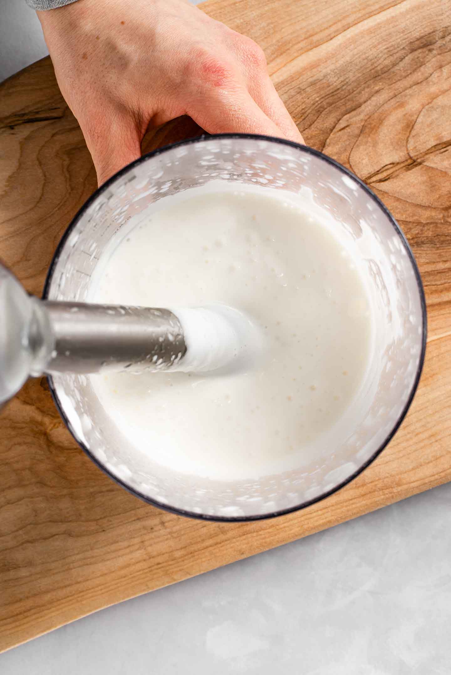 Top down view of quick easy aquafaba mayo in a tall container with an immersion blender submerged.