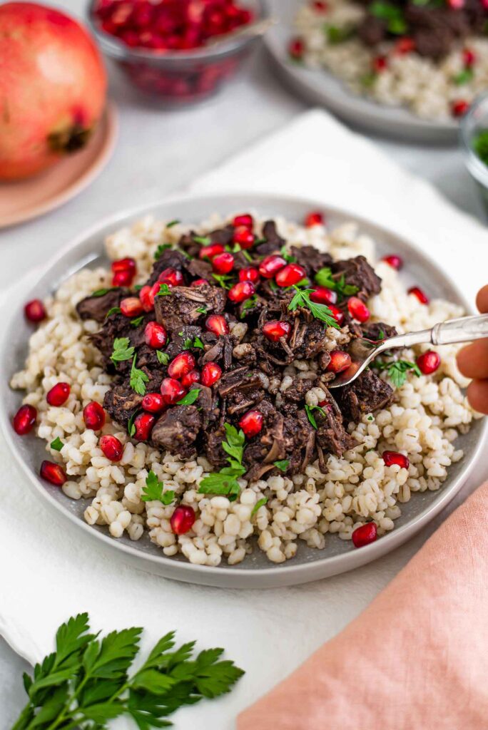 A fork scoops into the finished pomegranate jackfruit fesenjan dish.