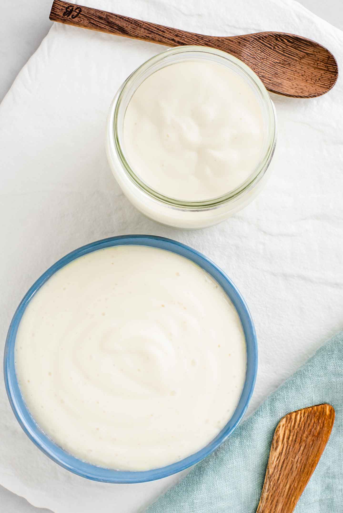 Top down view of oil-free mayonnaise made ahead of time in a jar wit a thicker consistency and mayonnaise straight out of the blender in a small bowl.