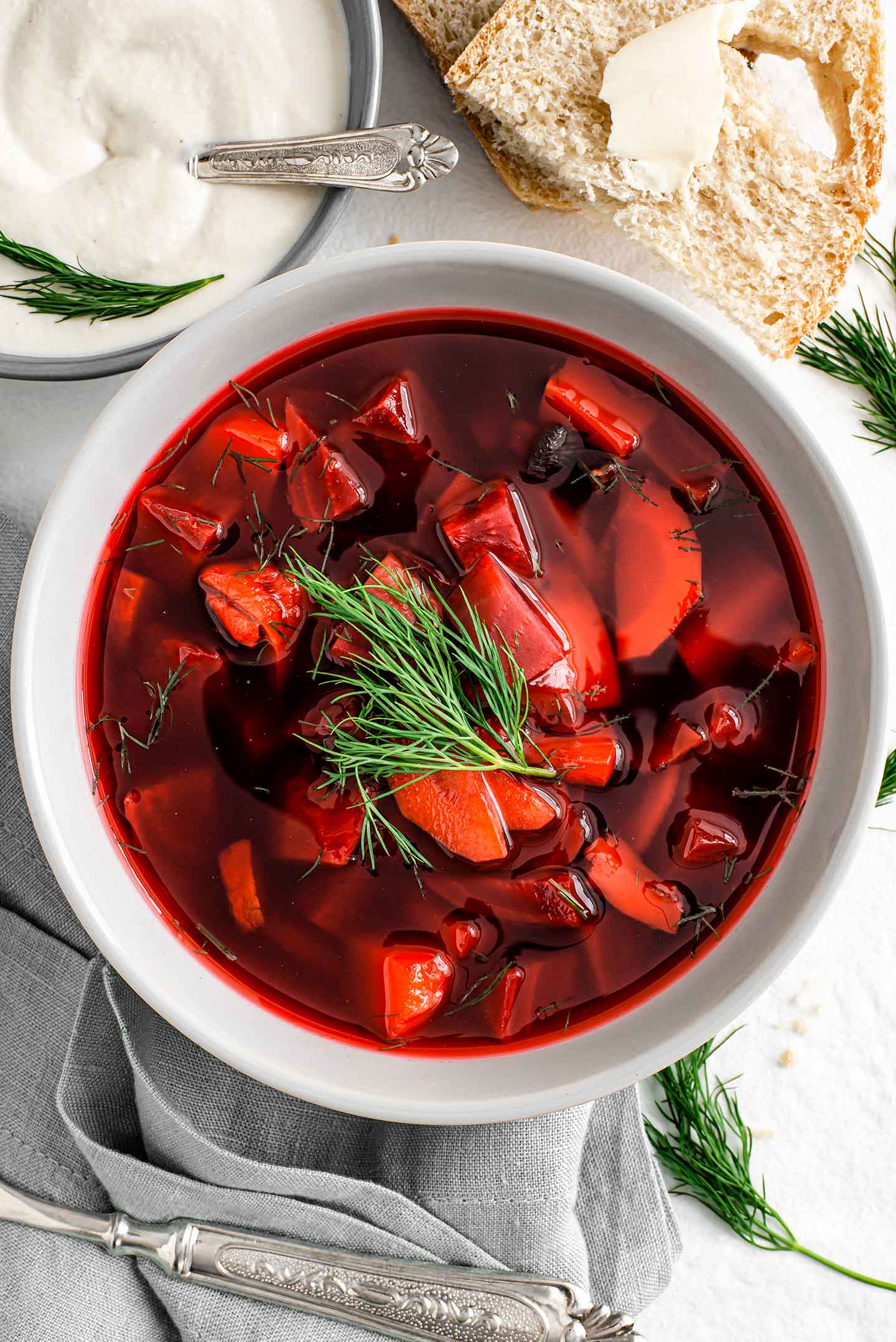 Top down view of vegan borscht in a bowl. Chunky beets, potatoes, carrot, and mushrooms are visible through the red broth. A sprig of fresh dill garnishes.