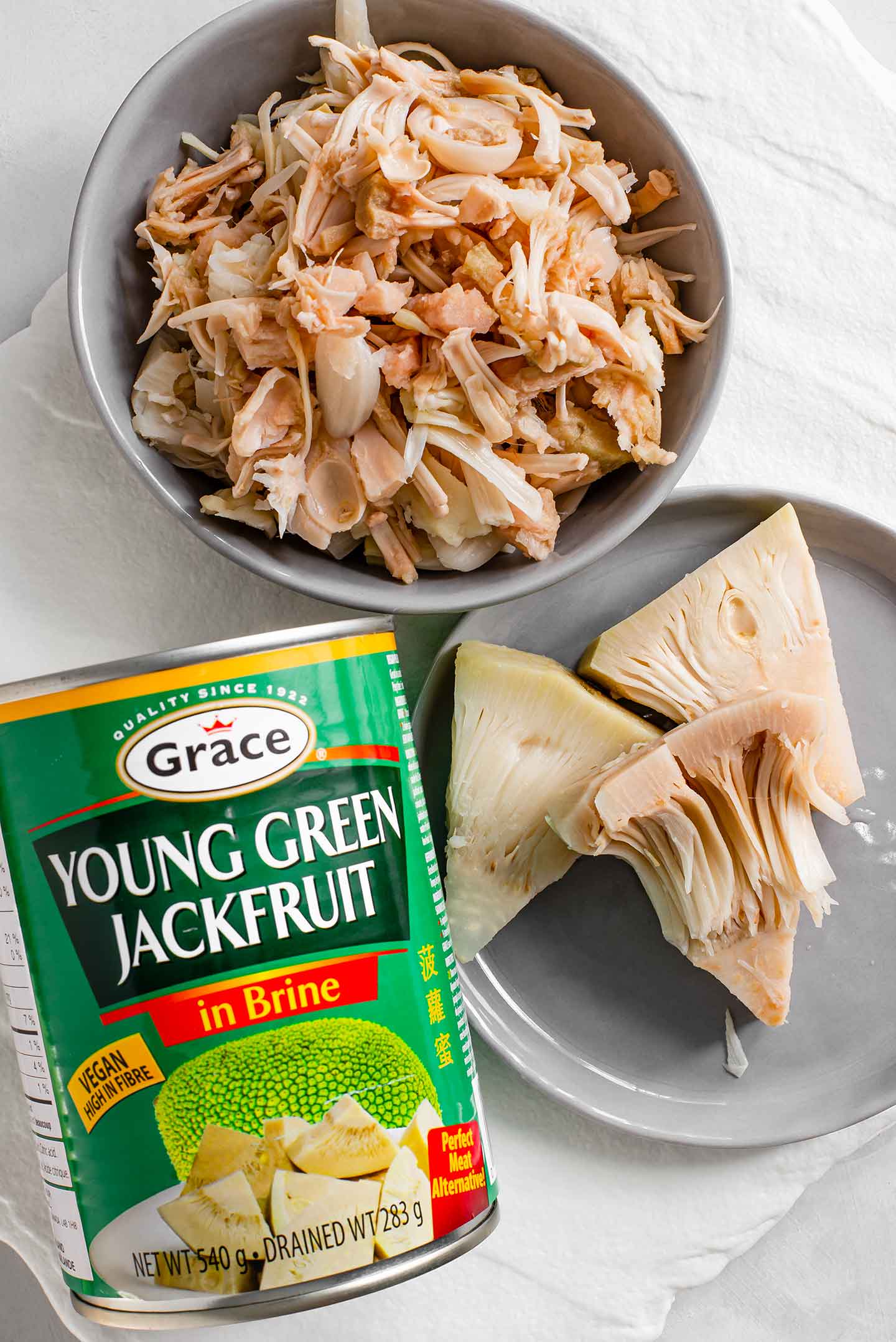 Top down view of canned young green jackfruit. Three full pieces of young jackfruit are shown on a plate and another dish holds pulled jackfruit.