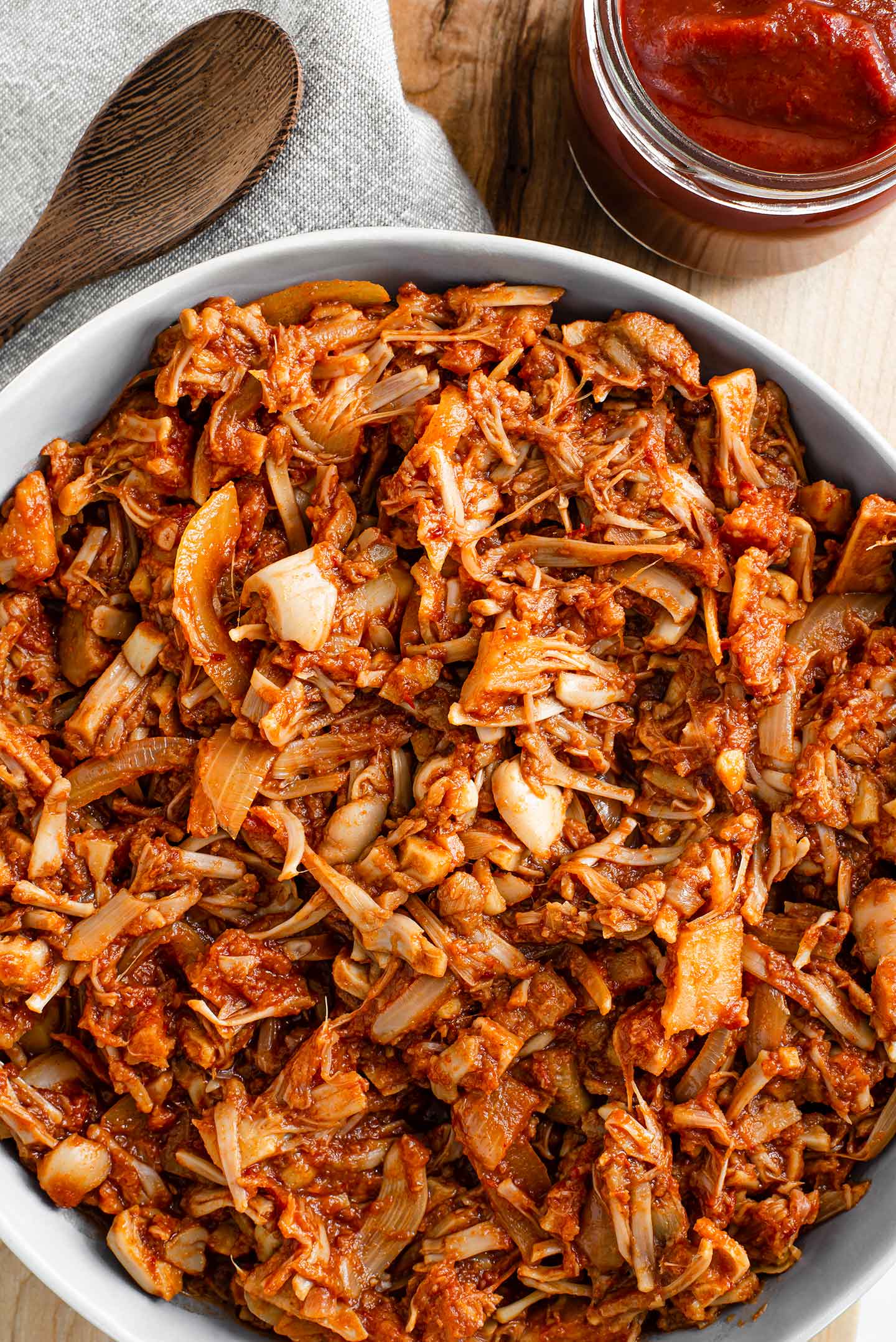 Top down view of BBQ pulled jackfruit in a serving bowl with extra chipotle BBQ sauce on the side.