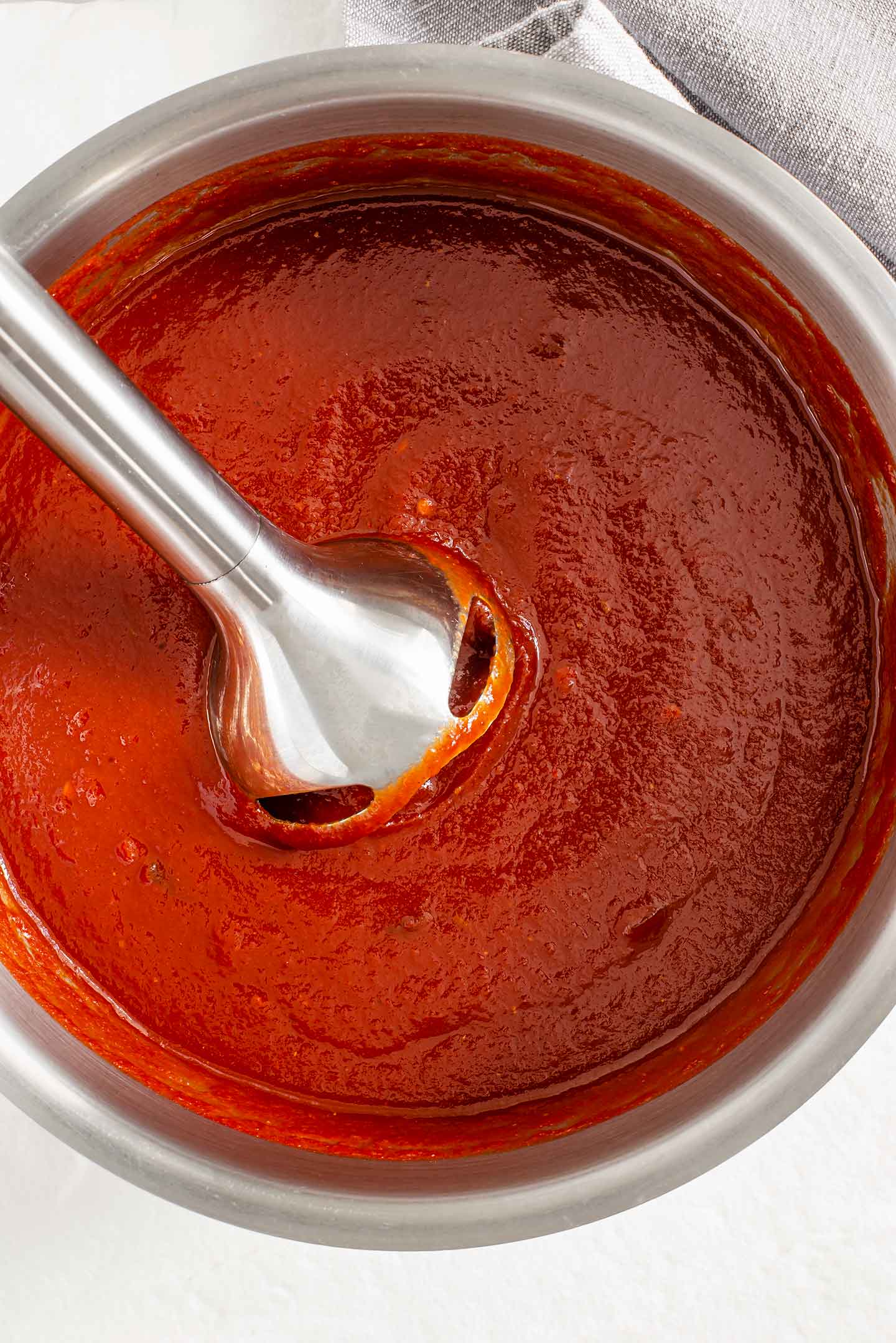 An immersion blender submerges into the heated barbecue sauce.