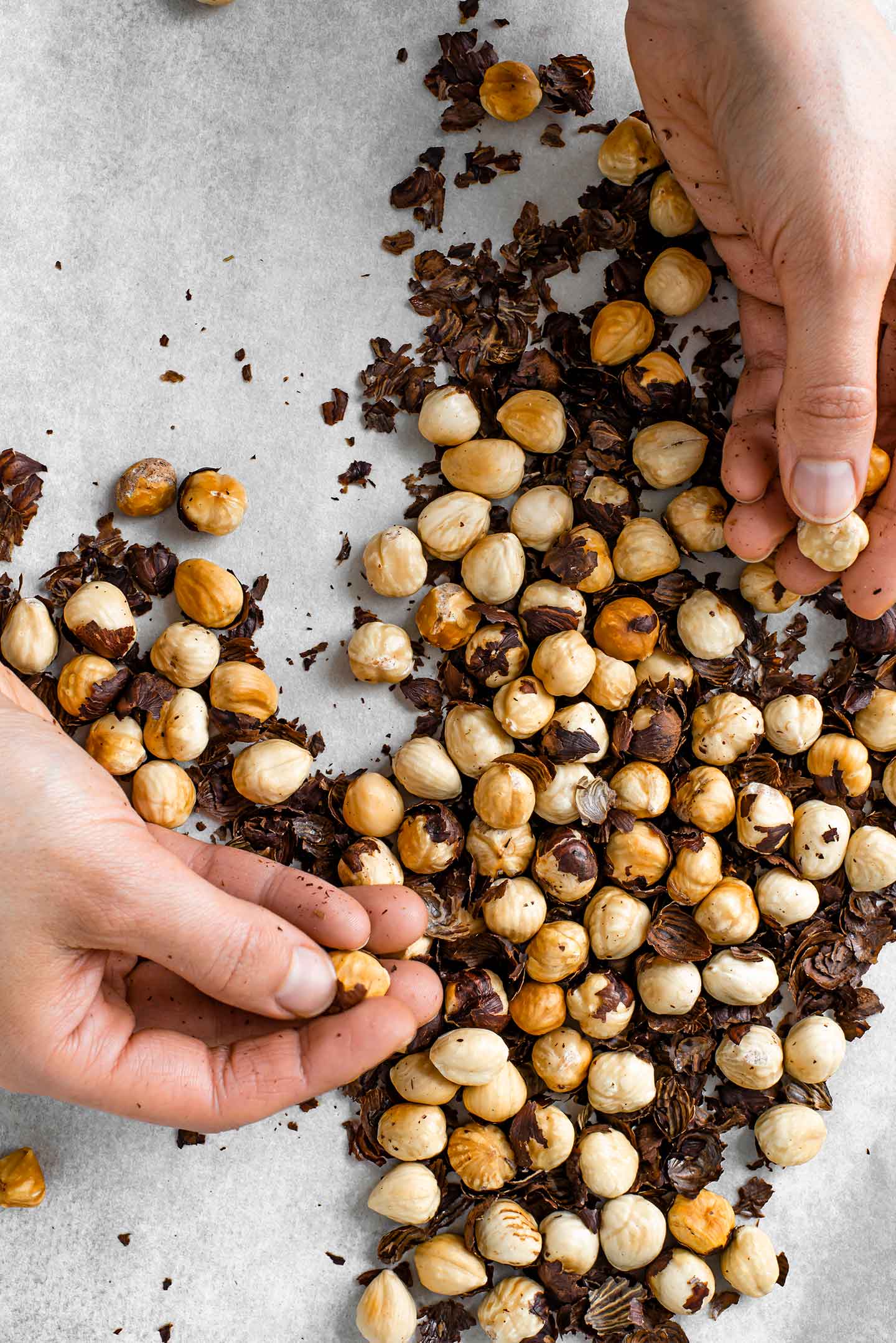 Top down view of hands rubbing the skins from the roasted hazelnuts.