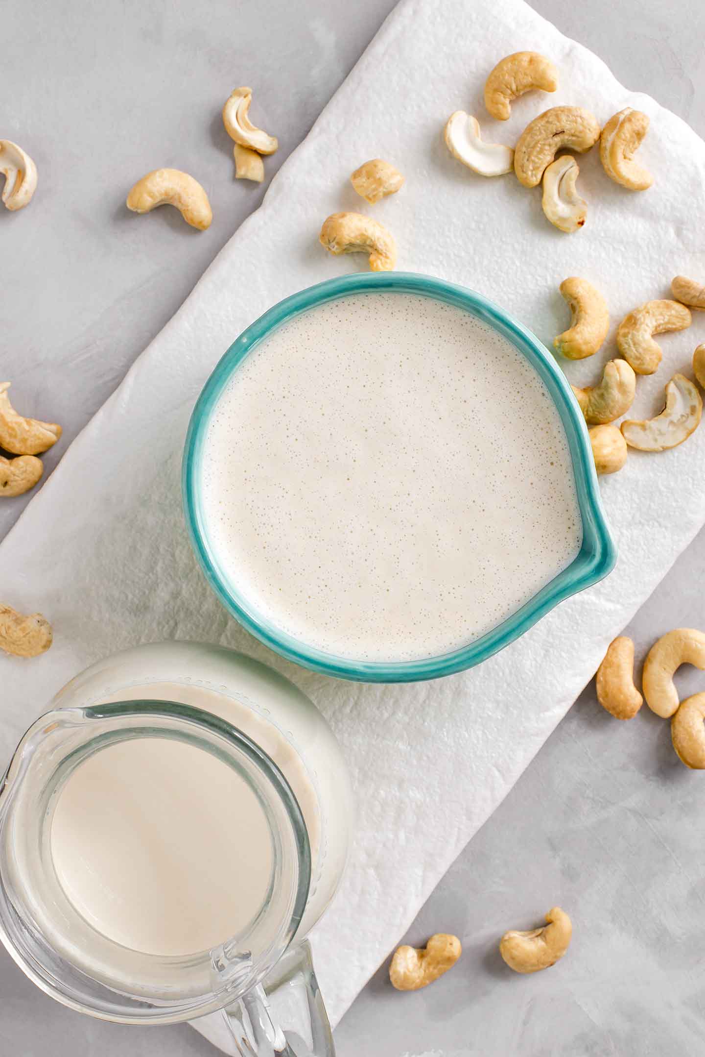 Top down view of thick cashew cream in a jar with raw cashews and milk surrounding.
