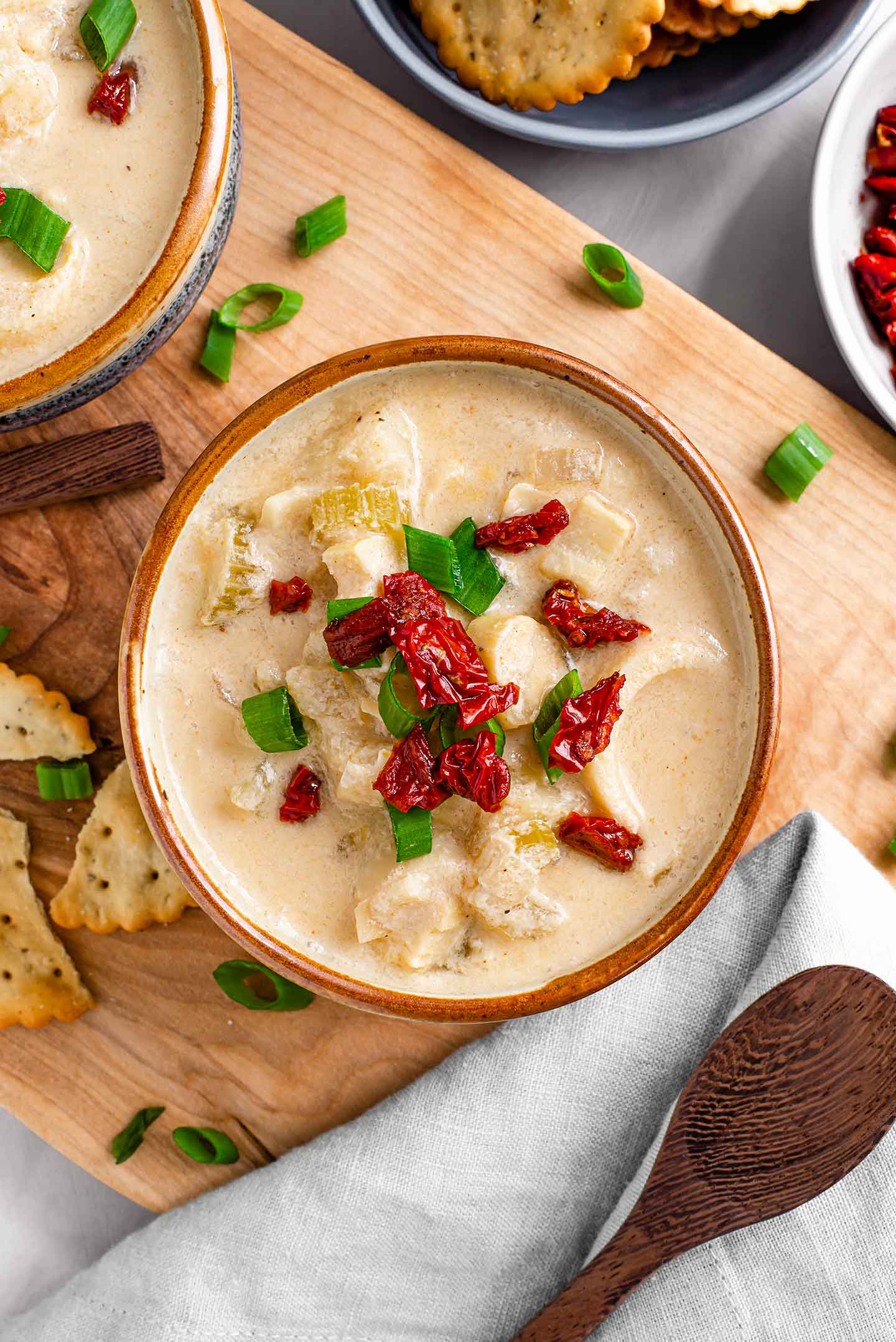 Top down view of a creamy hearty chowder in a bowl topped with sun-dried tomato bits and green onion.