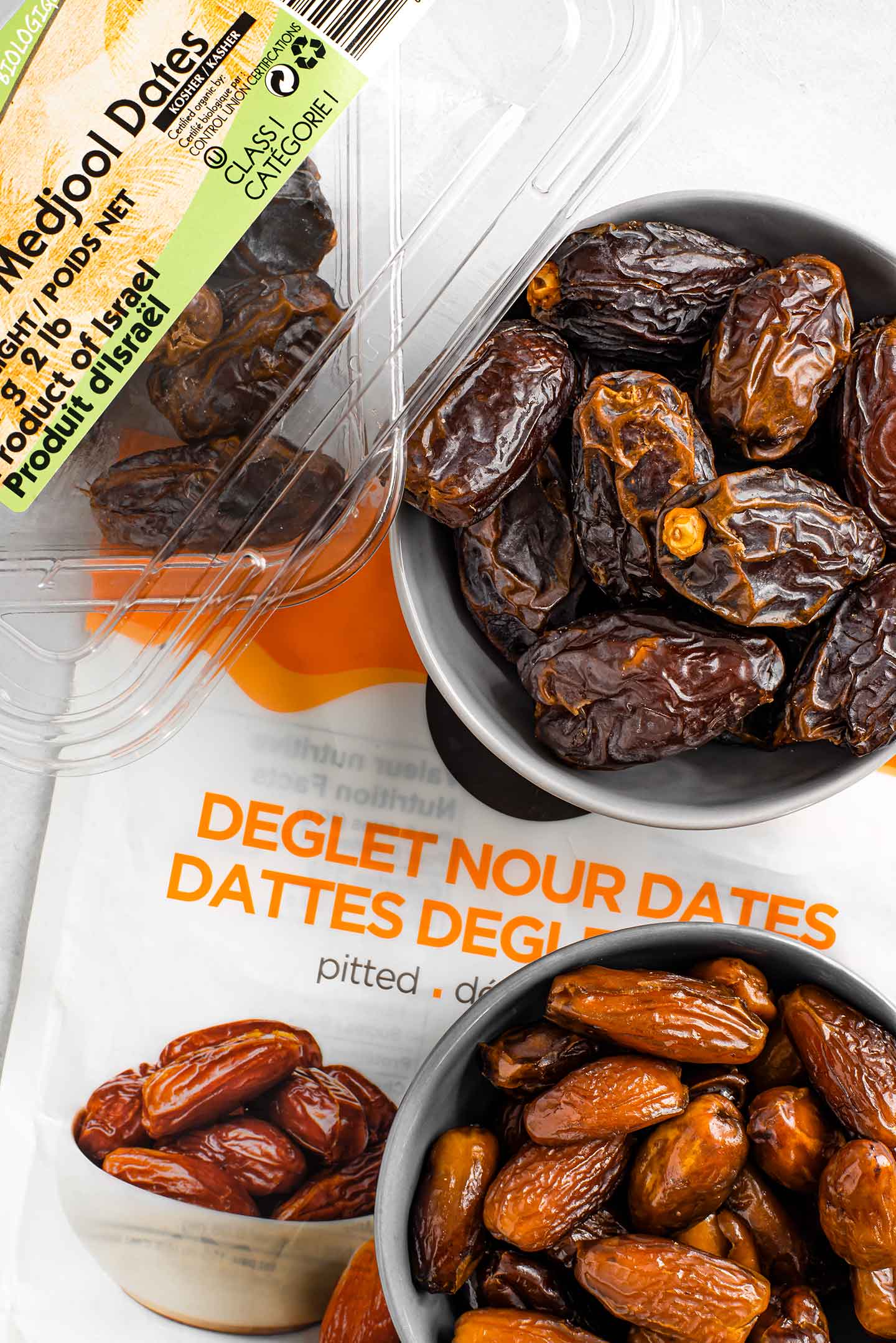 Top down view of large medjool dates and their packaging. Next to; smaller, lighter in colour, deglet nour dates and their packaging.