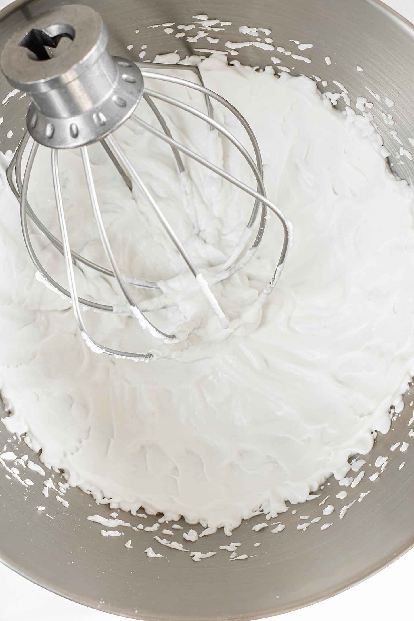 Top down view of coconut whipped cream in a metal mixing bowl with the whisk attachment in the cream