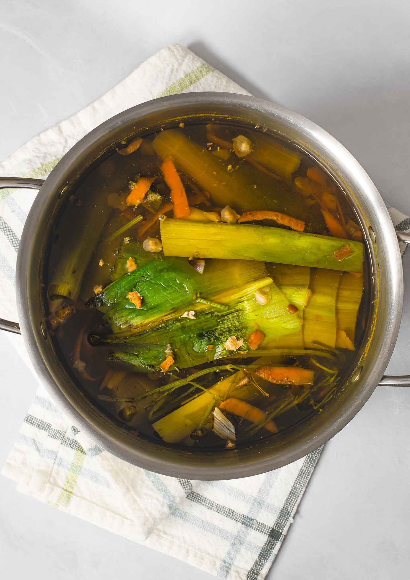 Top down view of homemade vegetable broth, before the vegetables have been strained, in a large pot with a dish towel underneath