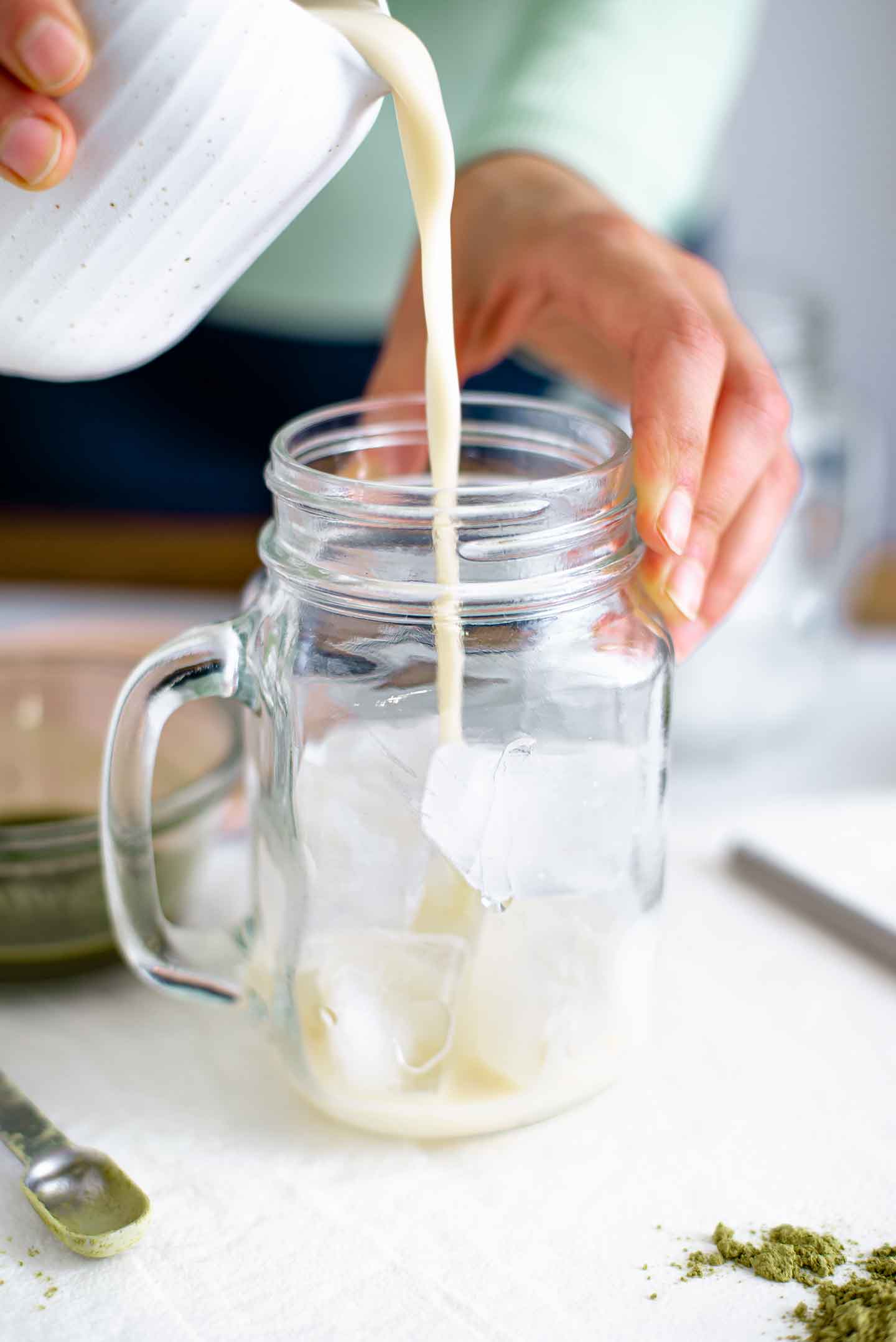 Side view of a hand pouring milk into a glass mug filled with ice.