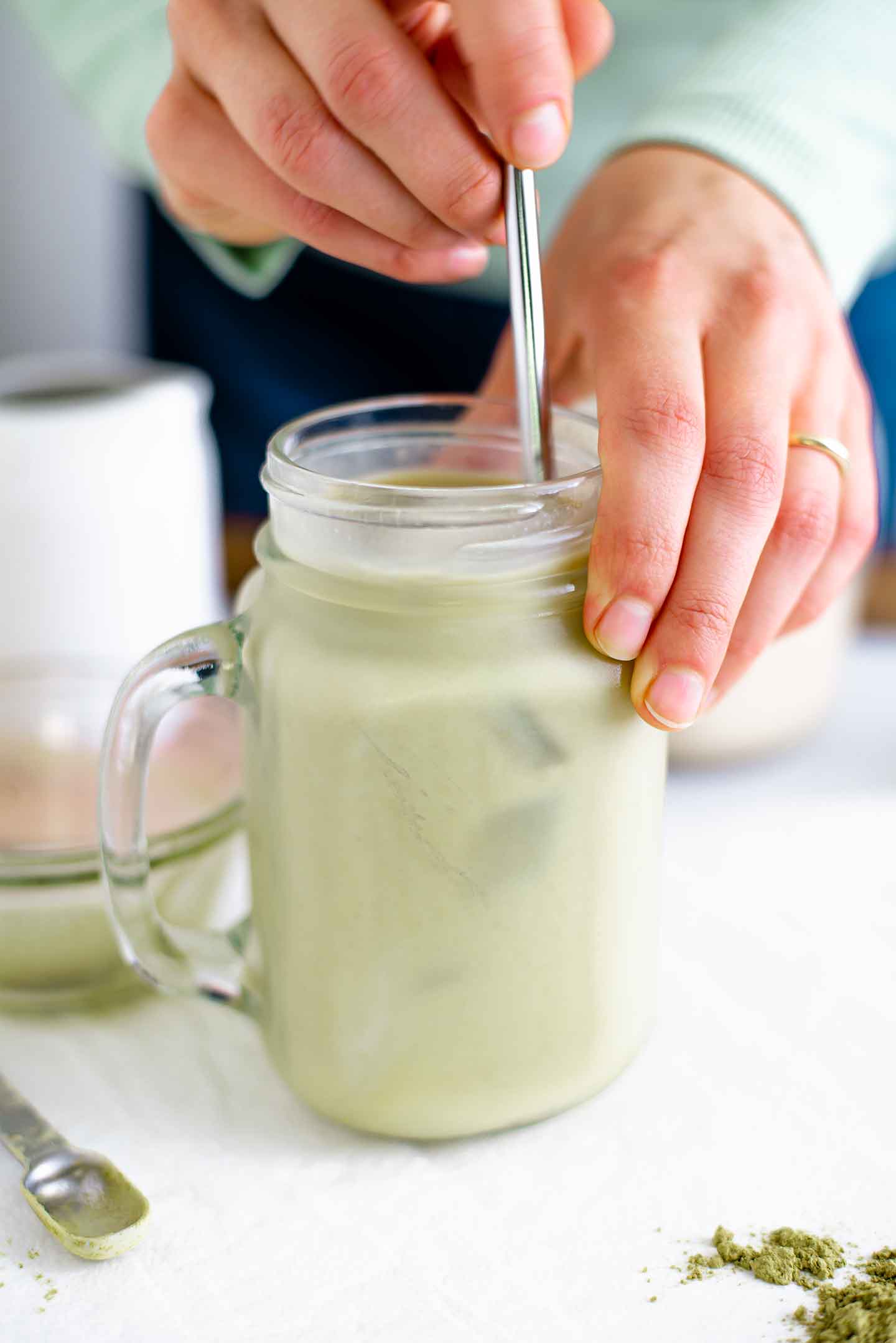 Hands stir a stainless steel straw through a light green iced matcha latte.