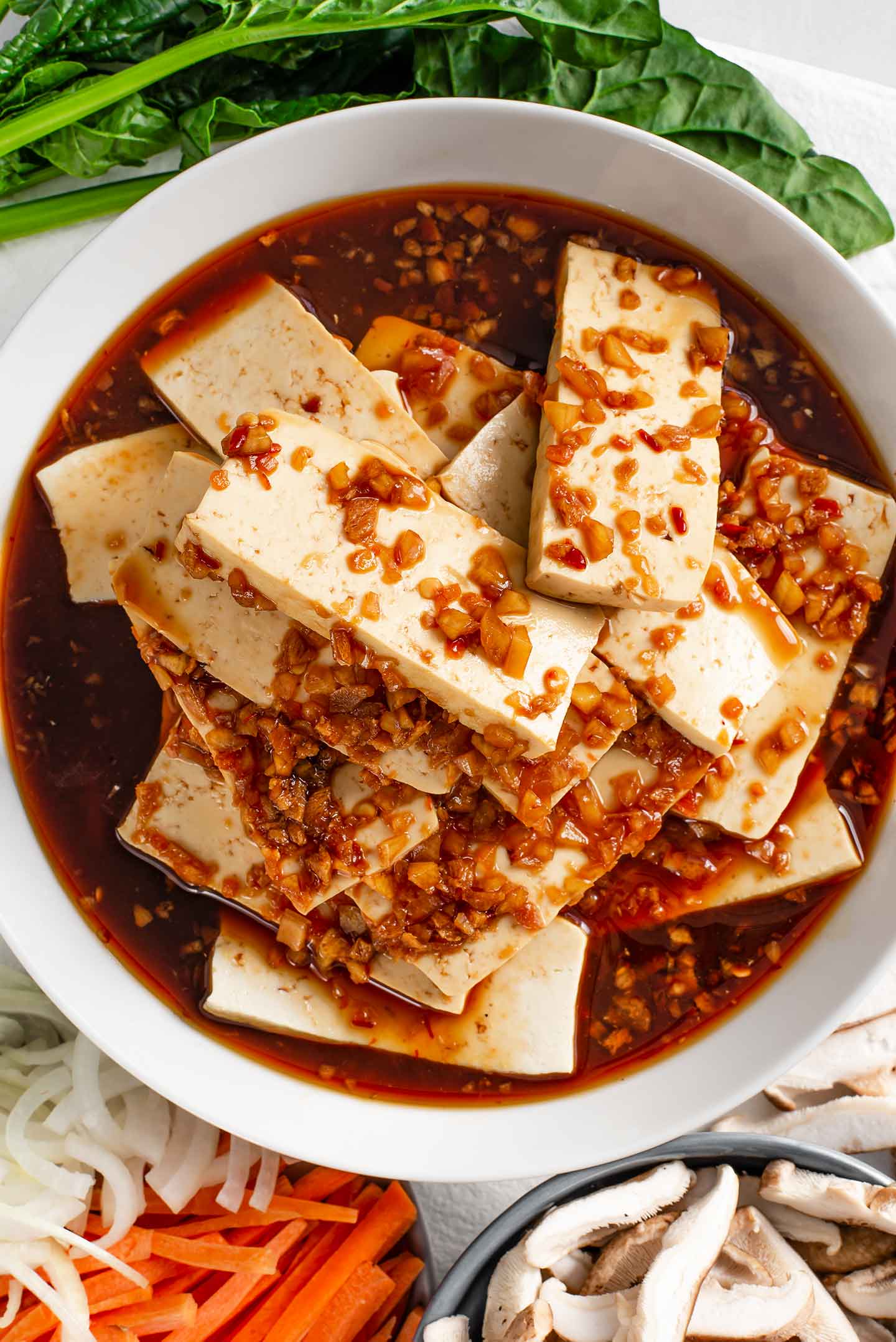 Top down view of sliced tofu in a shallow dish with a ginger, garlic, sweet and spicy sauce.