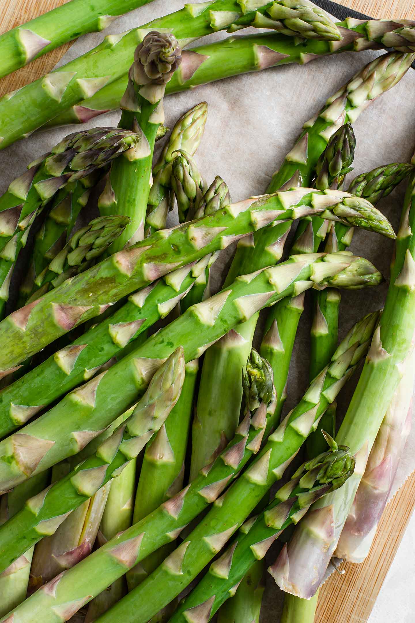 Top down view of long stalks of asparagus on a wooden tray.