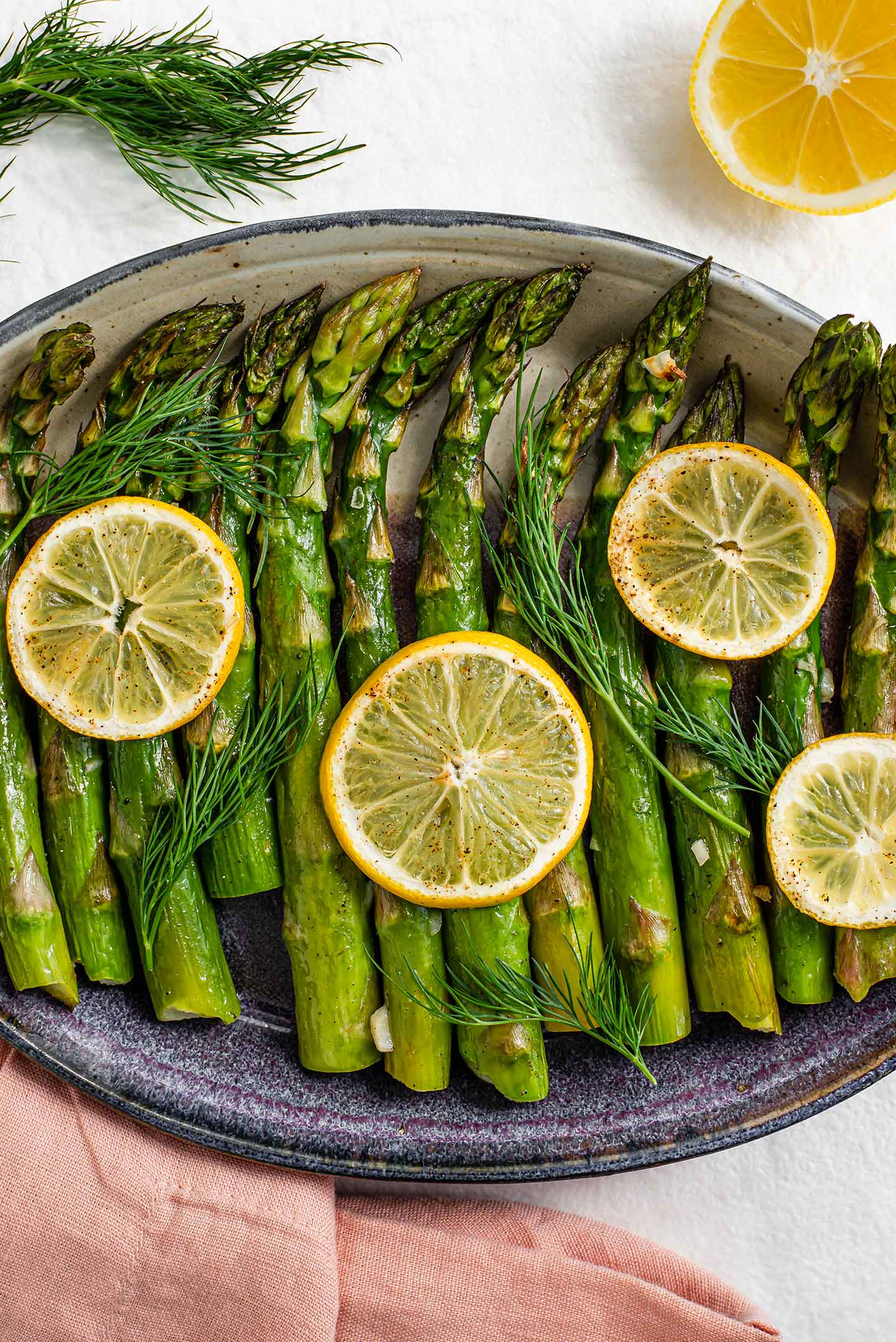 Top down view of lemon roasted asparagus in a serving platter with roasted lemon slices and fresh dill to garnish