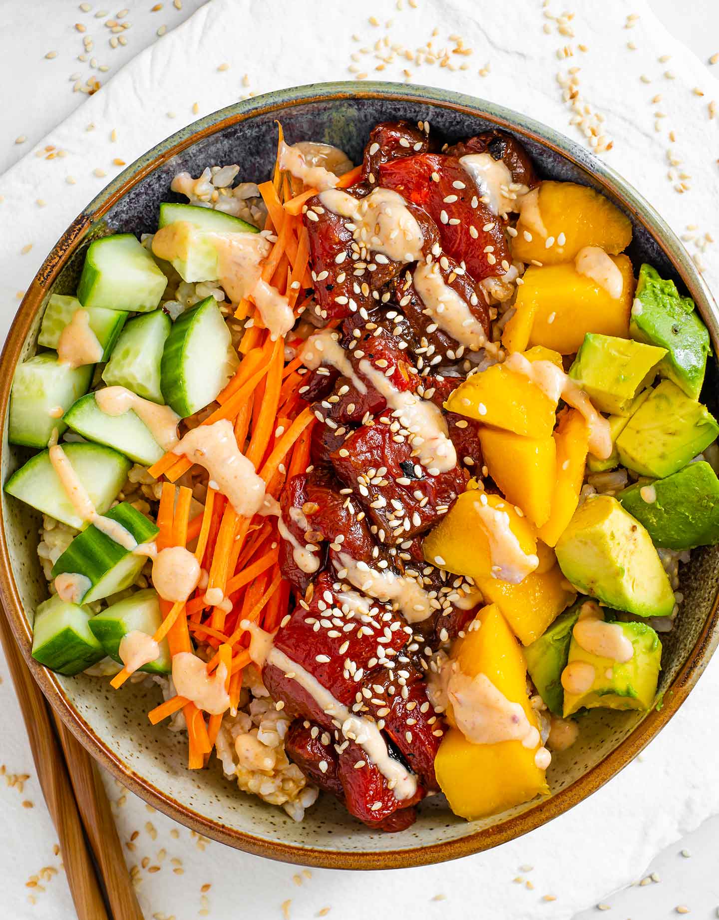 Top down view of a poke bowl with the colourful ingredients in straight lines. Sesame seeds are scattered on the tray beneath the bowl.