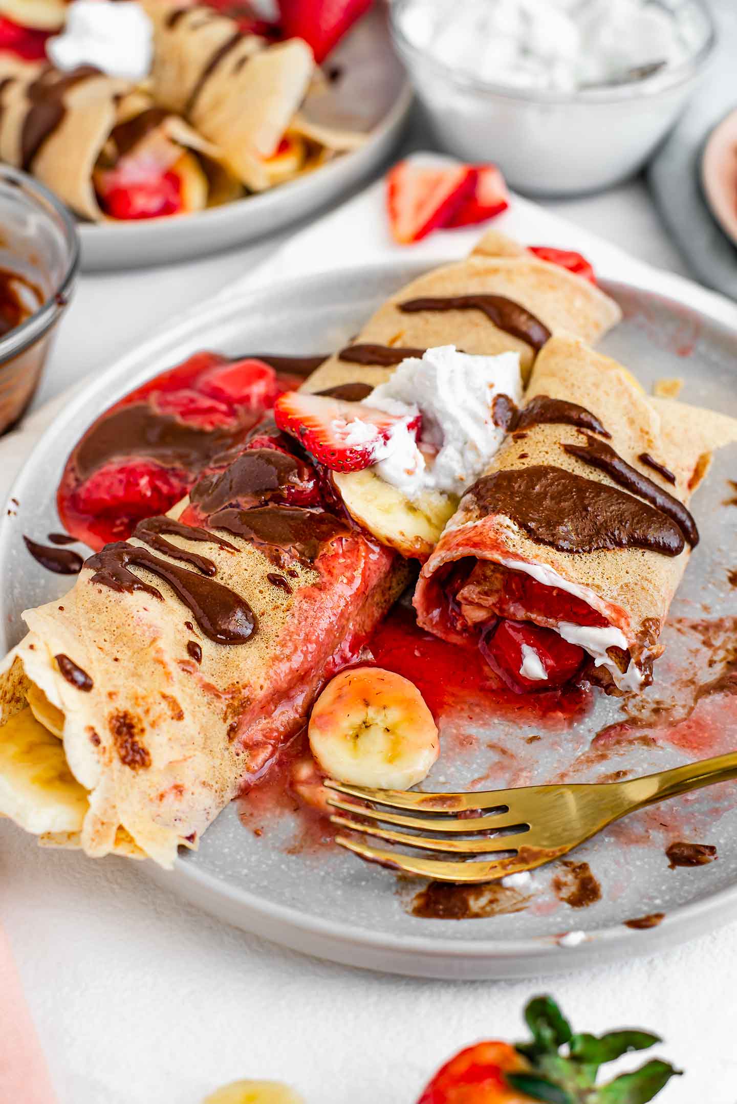 Side view of a fork resting on a plate of crepes with one crepe half eaten exposing the warm strawberry filling inside.