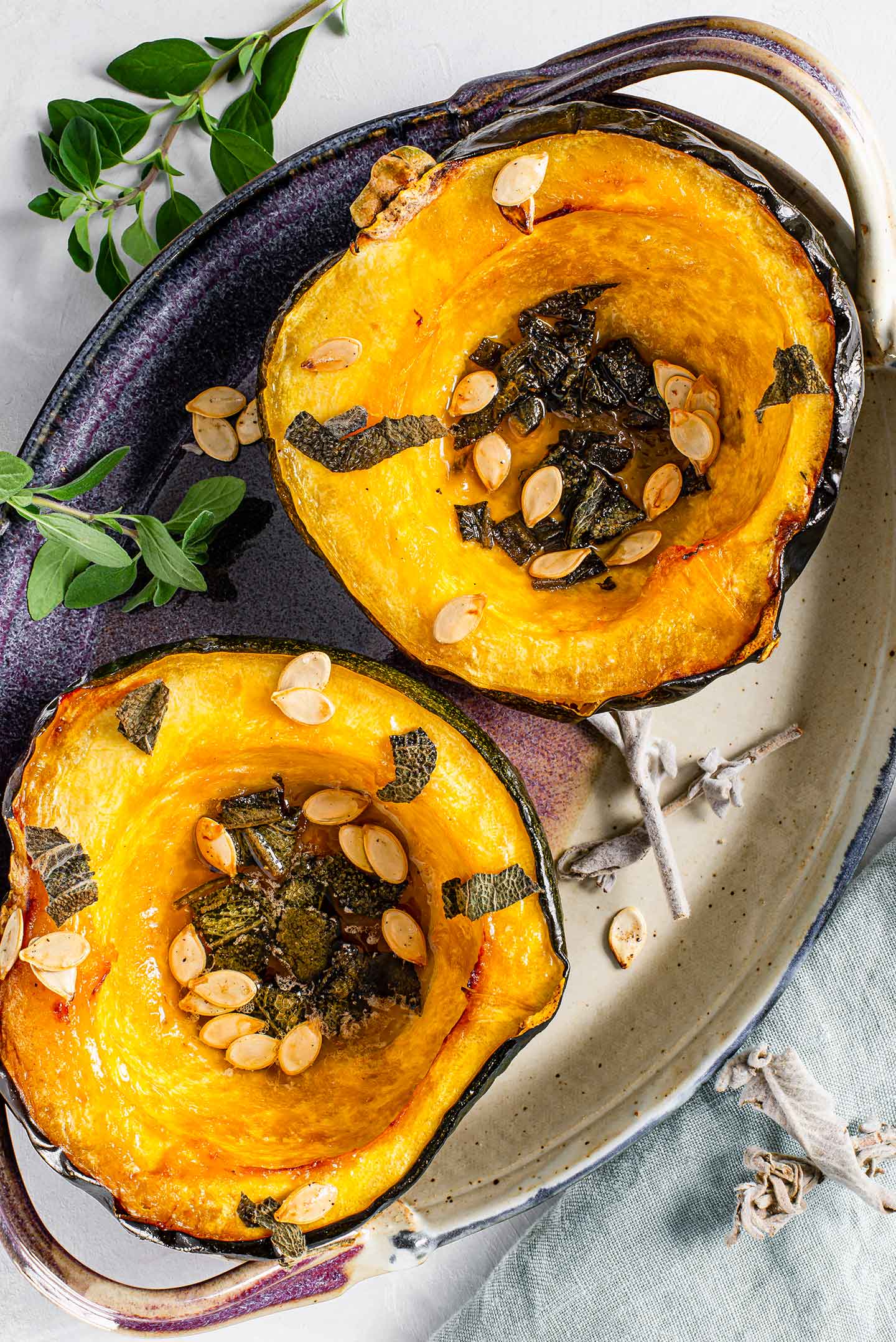 Top down view of two roasted acorn squash halves caramelized with maple syrup and sprinkled with sage and roasted squash seeds.