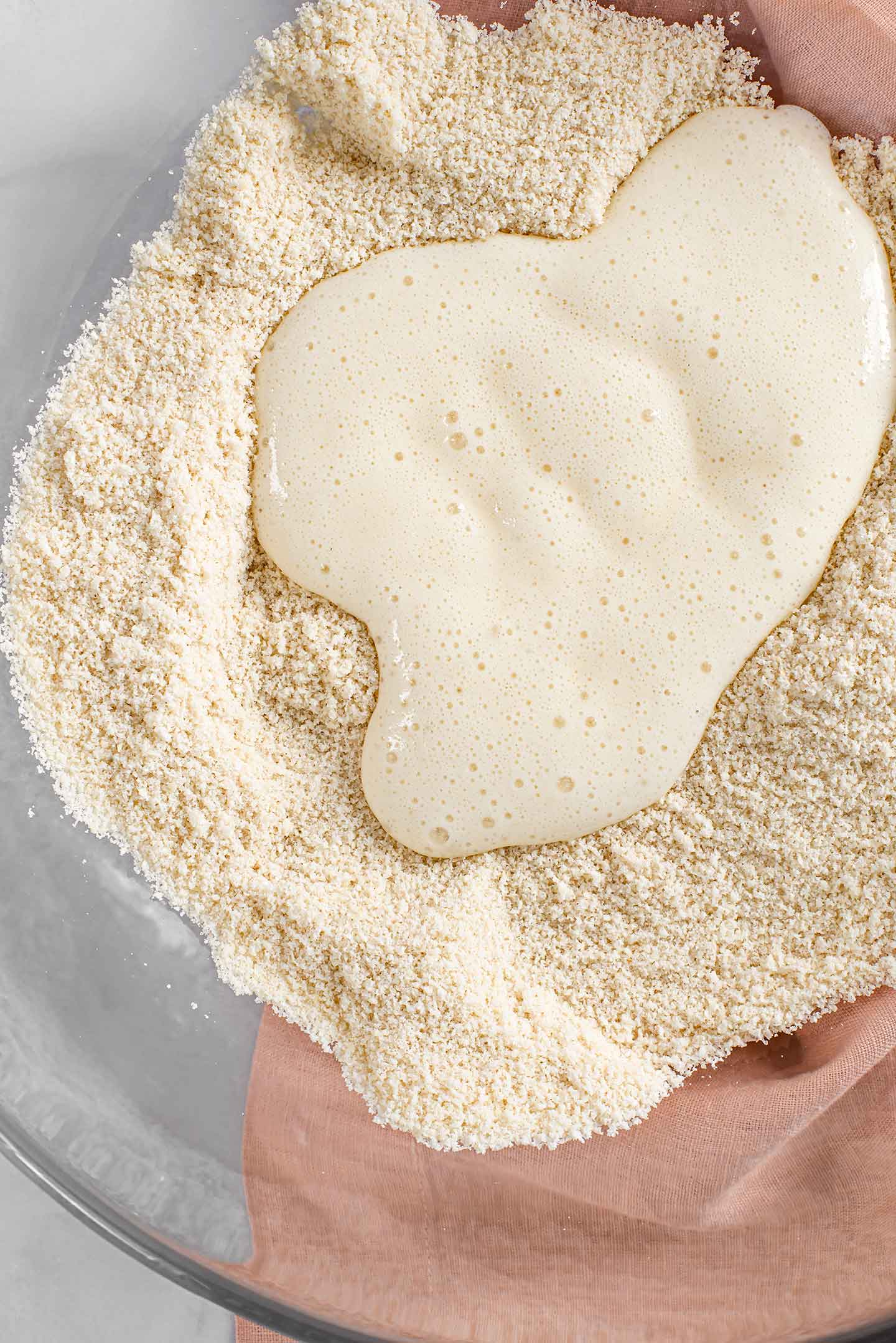 Top down view of almond flour in a mixing bowl with the wet ingredients being poured over top.