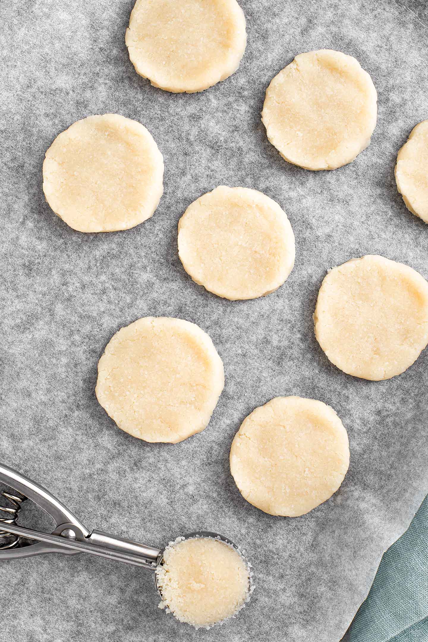 Top down view of the dough formed into rounds on a baking tray. A cookie scoop is full of more packed dough.