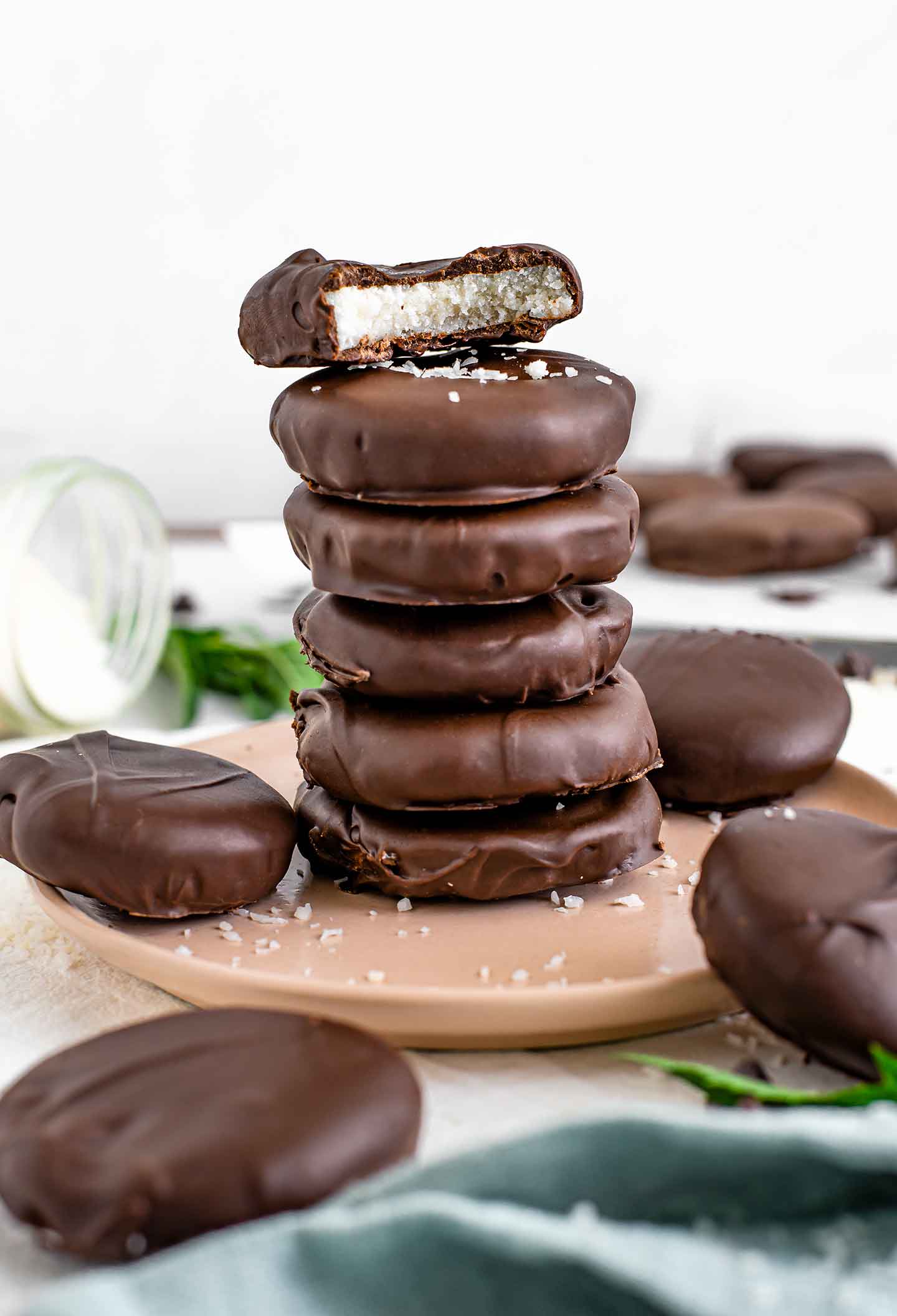 Side view of coconut peppermint patties scattered and stacked on a plate. The top patty has a bite missing from it, revealing the firm coconut interior.