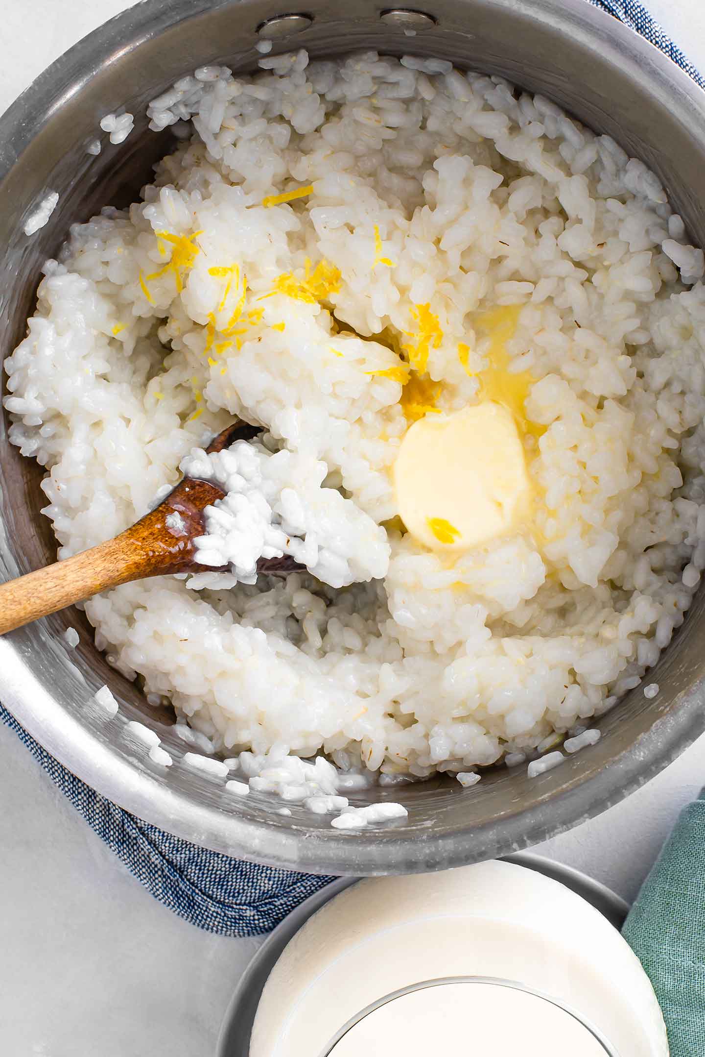 Top down view of butter melting into white rice. Lemon zest sits on the top of the rice and a wooden spoon rests in the pot.