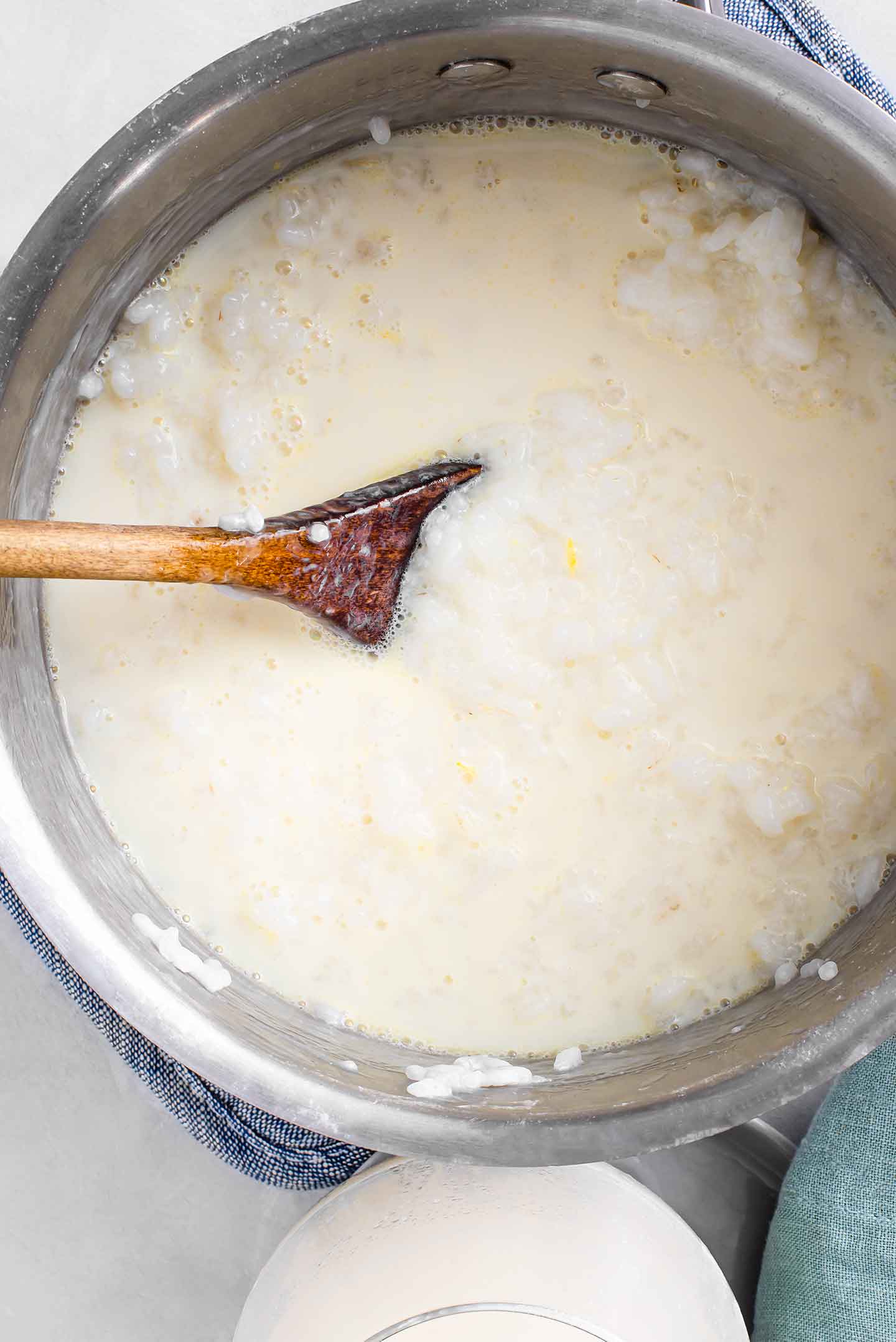 Top down view of thick rice pudding in a medium pot with a wooden spoon resting in the mixture.