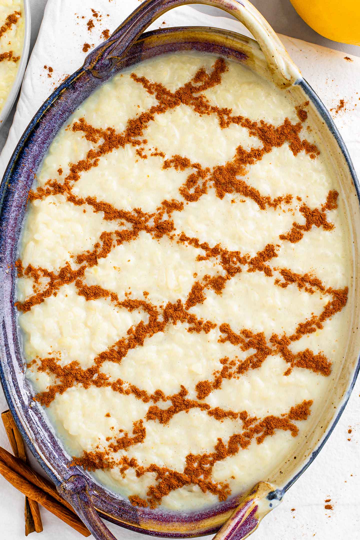 Top down view of Portuguese sweet rice in an oval dish decorated with a cinnamon criss cross pattern.