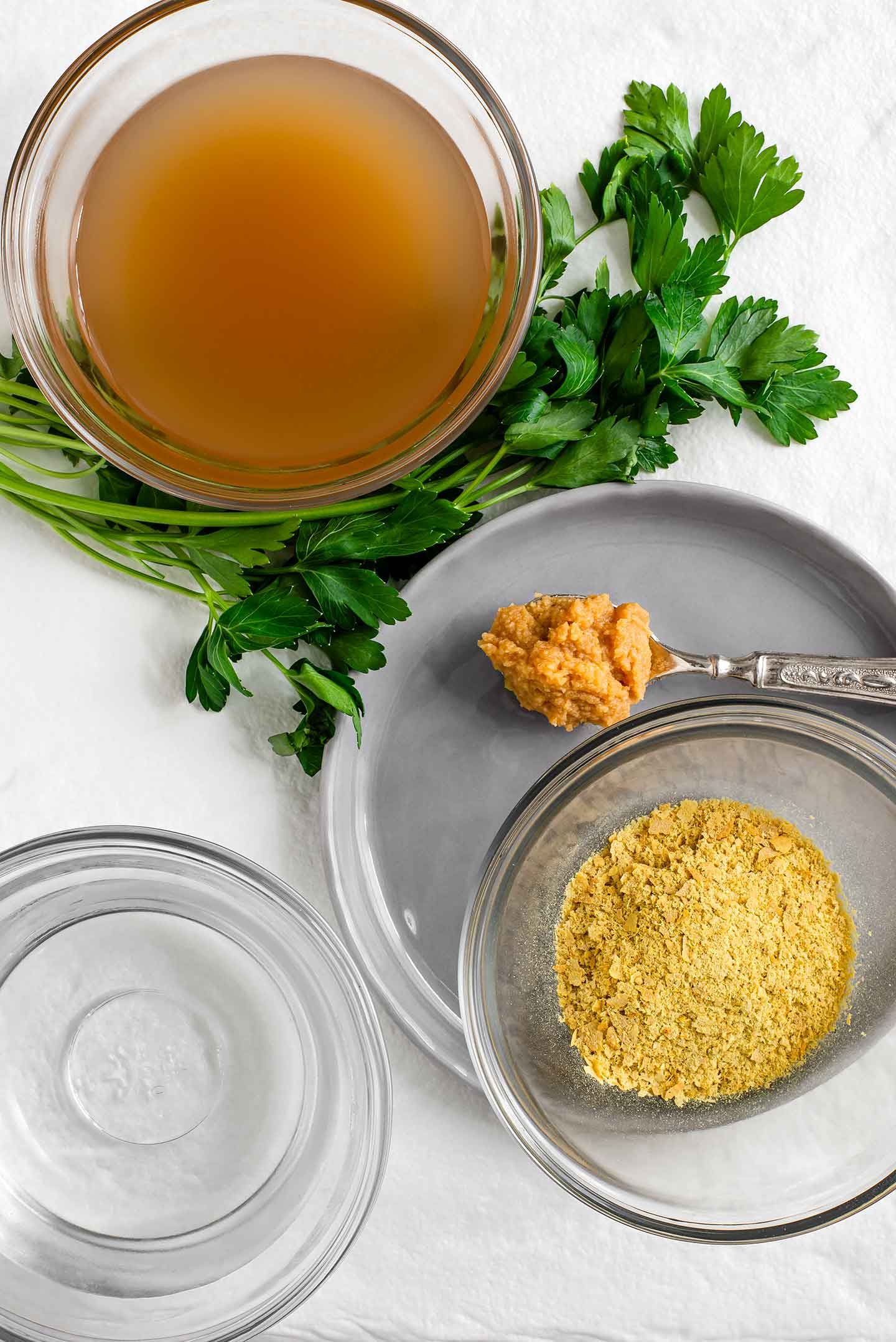 Top down view of apple cider vinegar, miso paste, nutritional yeast, fresh parsley, and water.