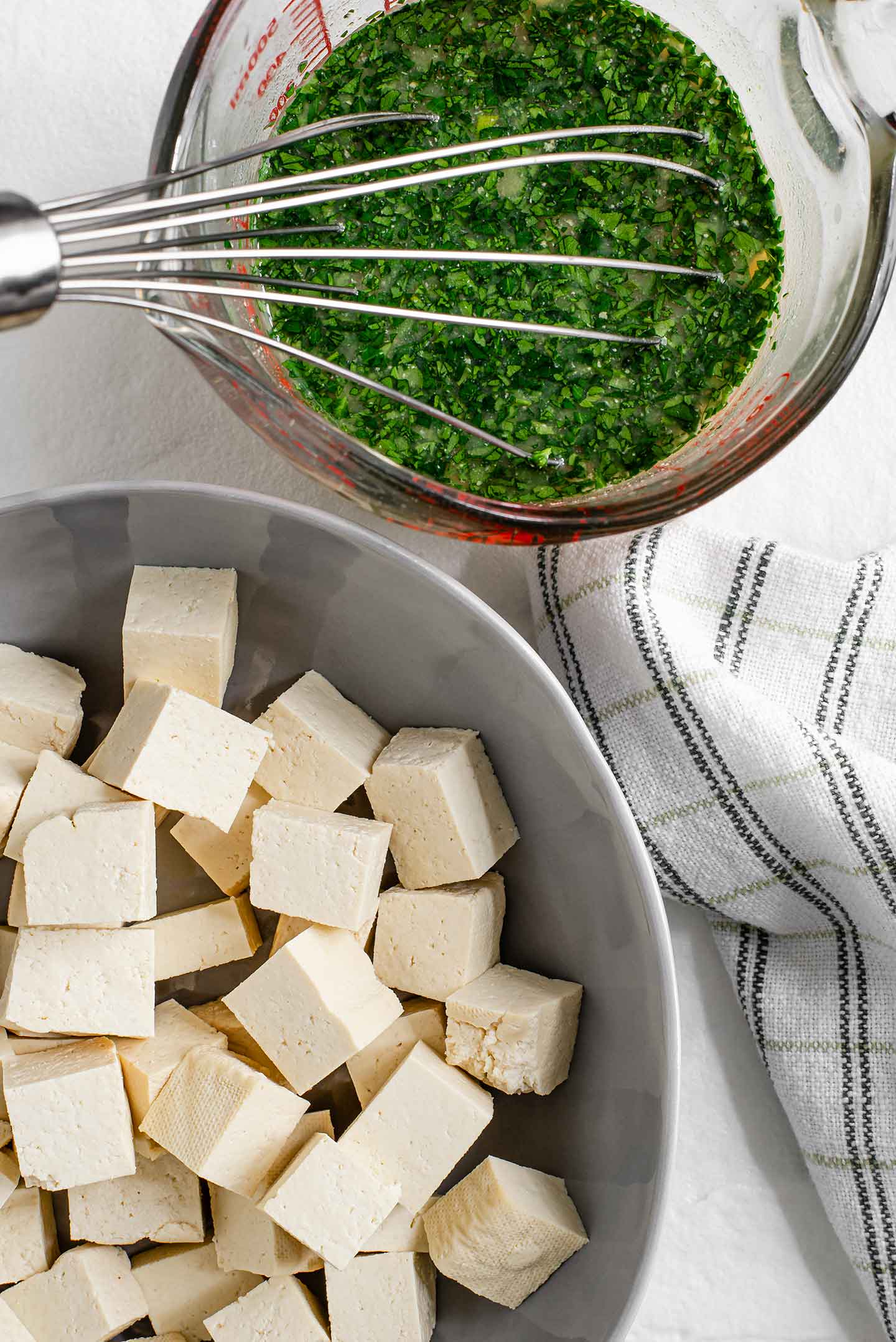 Top down view of tofu sliced into cubes and the feta dressing prepared in a small glass dish with a whisk.