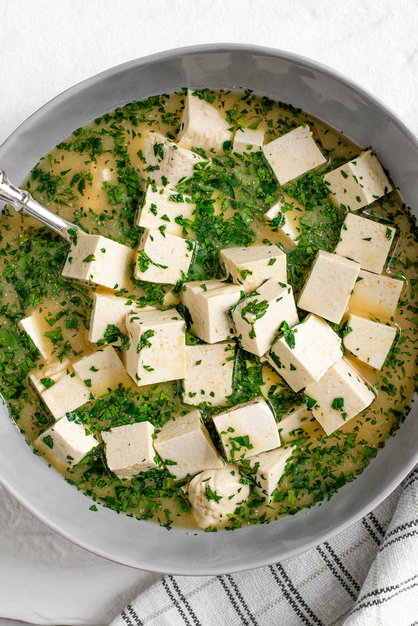 Top down view of quick and easy feta in a bowl with marinade and chopped parsley. A spoon sits in the middle of the feta cubes.