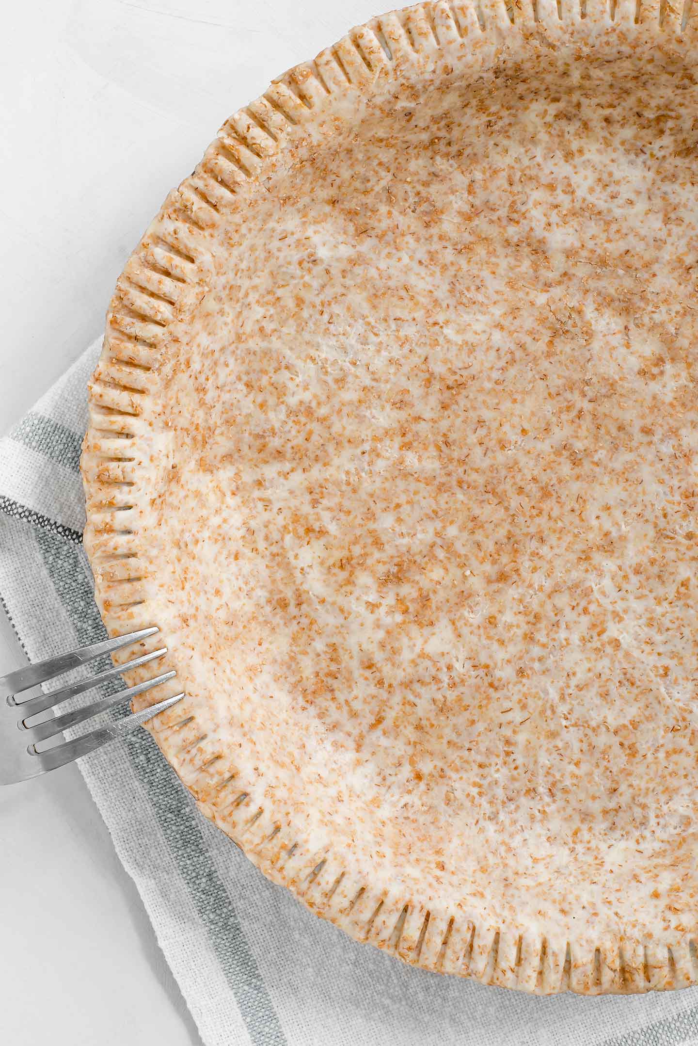 Top down view of an unbaked homemade whole wheat crust in a pie plate. A fork crimps the edges.