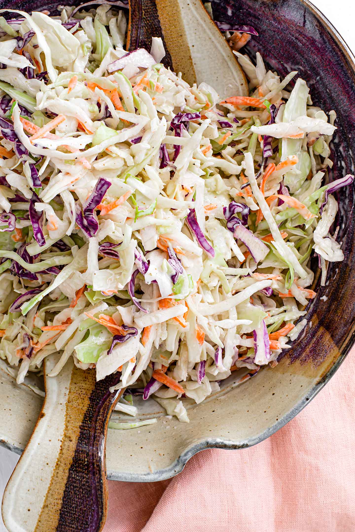 Top down view of a summery vegan coleslaw recipe in a ceramic salad bowl. Shredded green and red cabbage are mixed with shredded carrot and tossed in our sweet and tangy dressing.