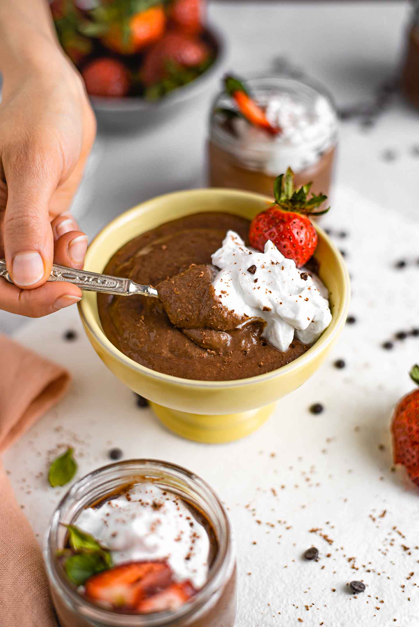 Side view of a hand using a spoon to scoop chocolate pudding topped with coconut whipped cream.