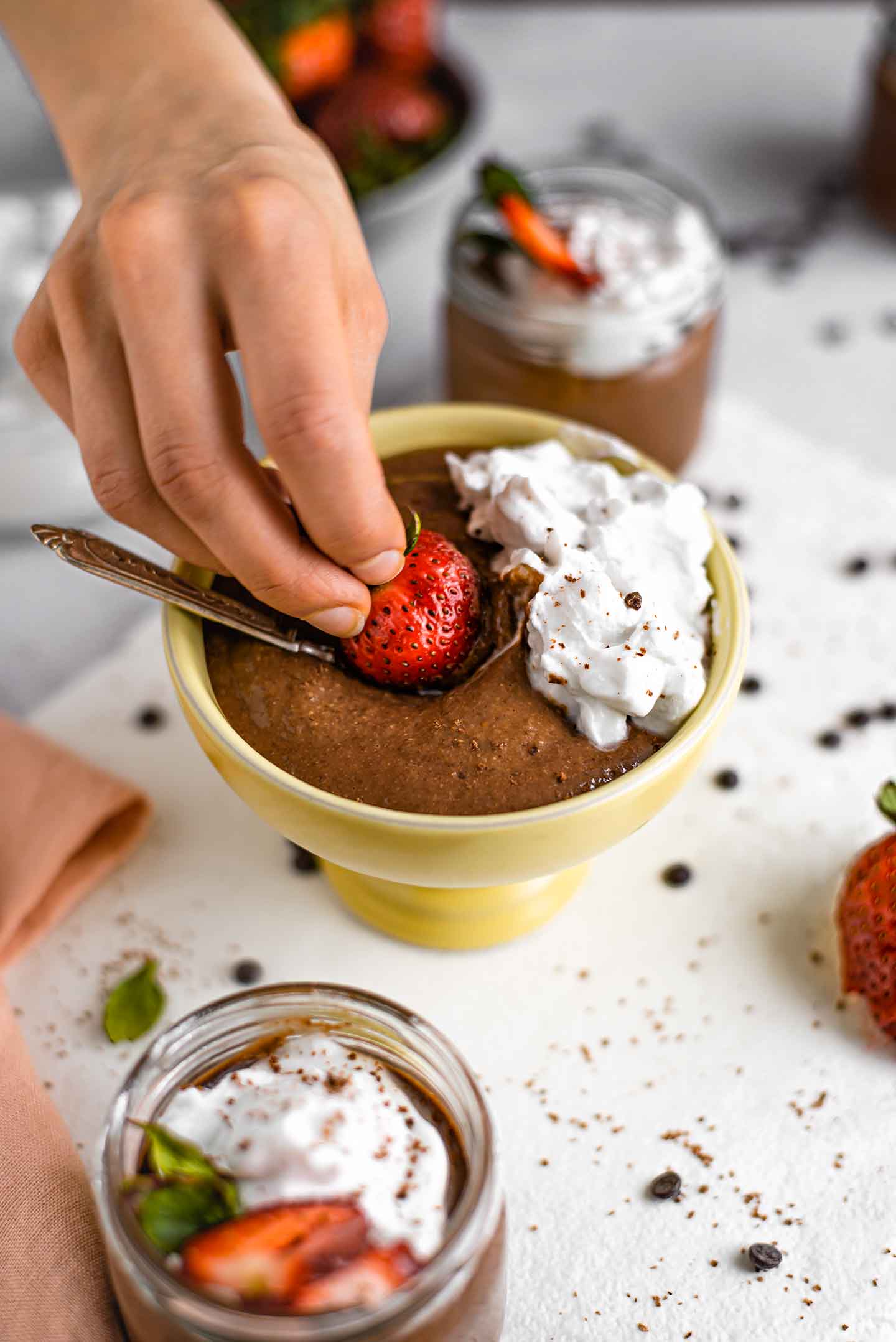 Side view of fingers dipping a strawberry into chocolate pudding and whipped cream.