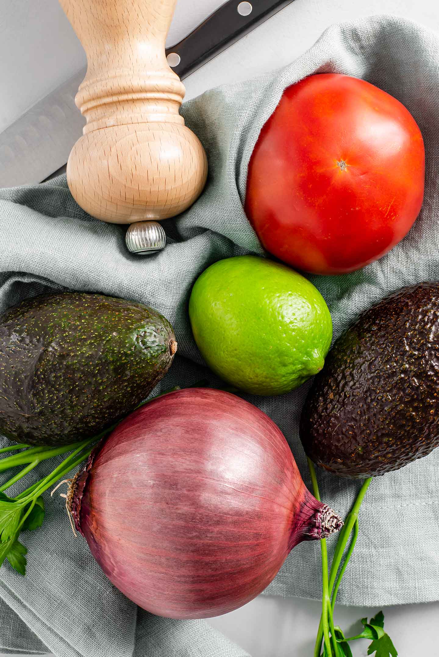 Top down view of guacamole ingredients. Two avocados, red onion, lime, tomato, cilantro and salt in a salt shaker.