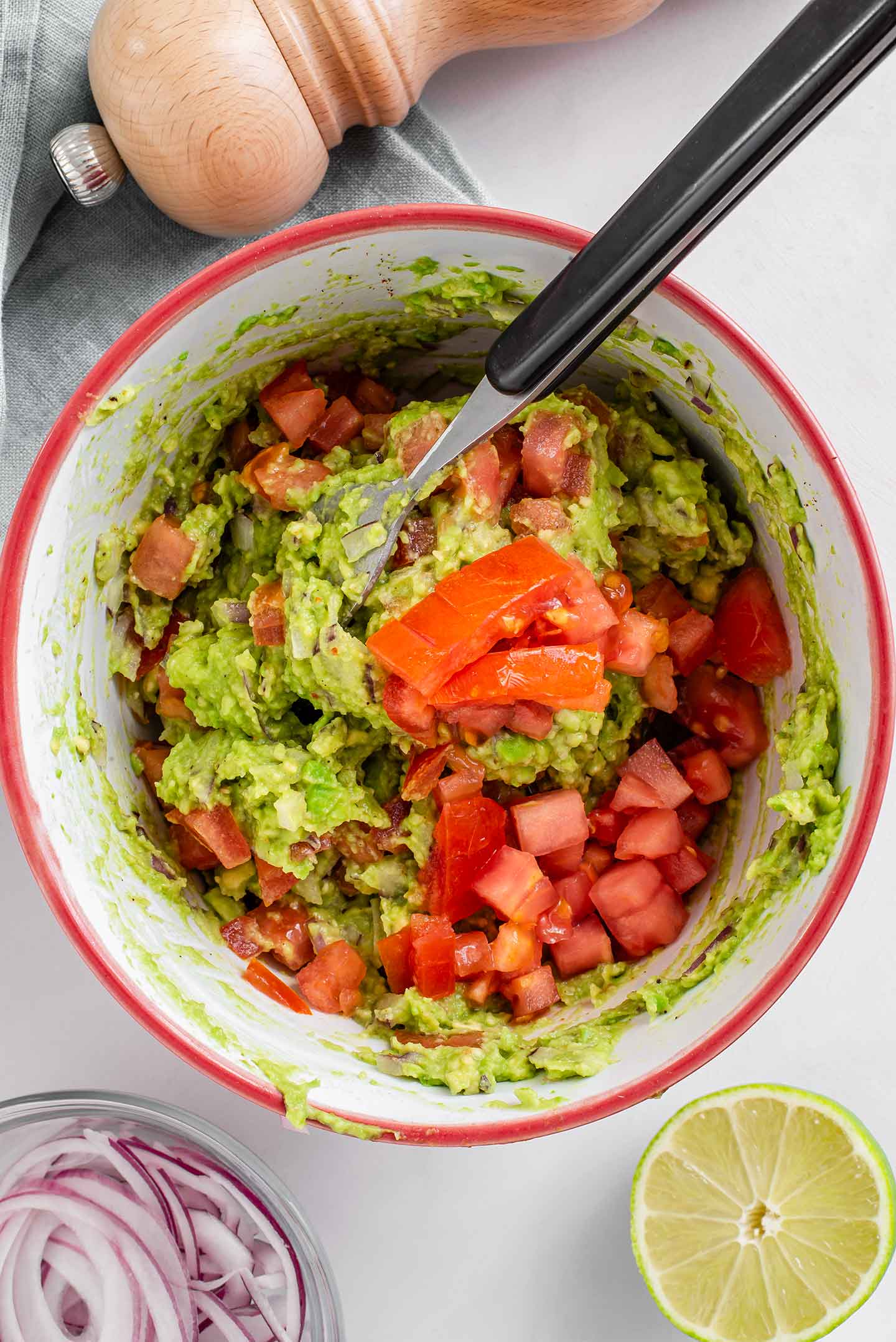 Top down view of mashed avocado in a bowl with diced tomato being stirred in.