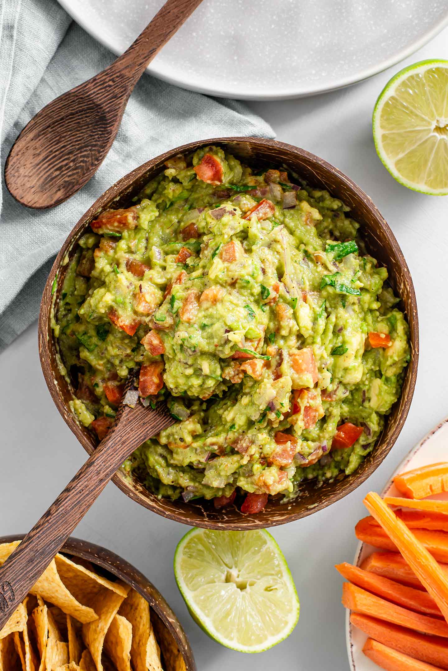 Top down view of timely guacamole in a coconut bowl with a bamboo spoon.