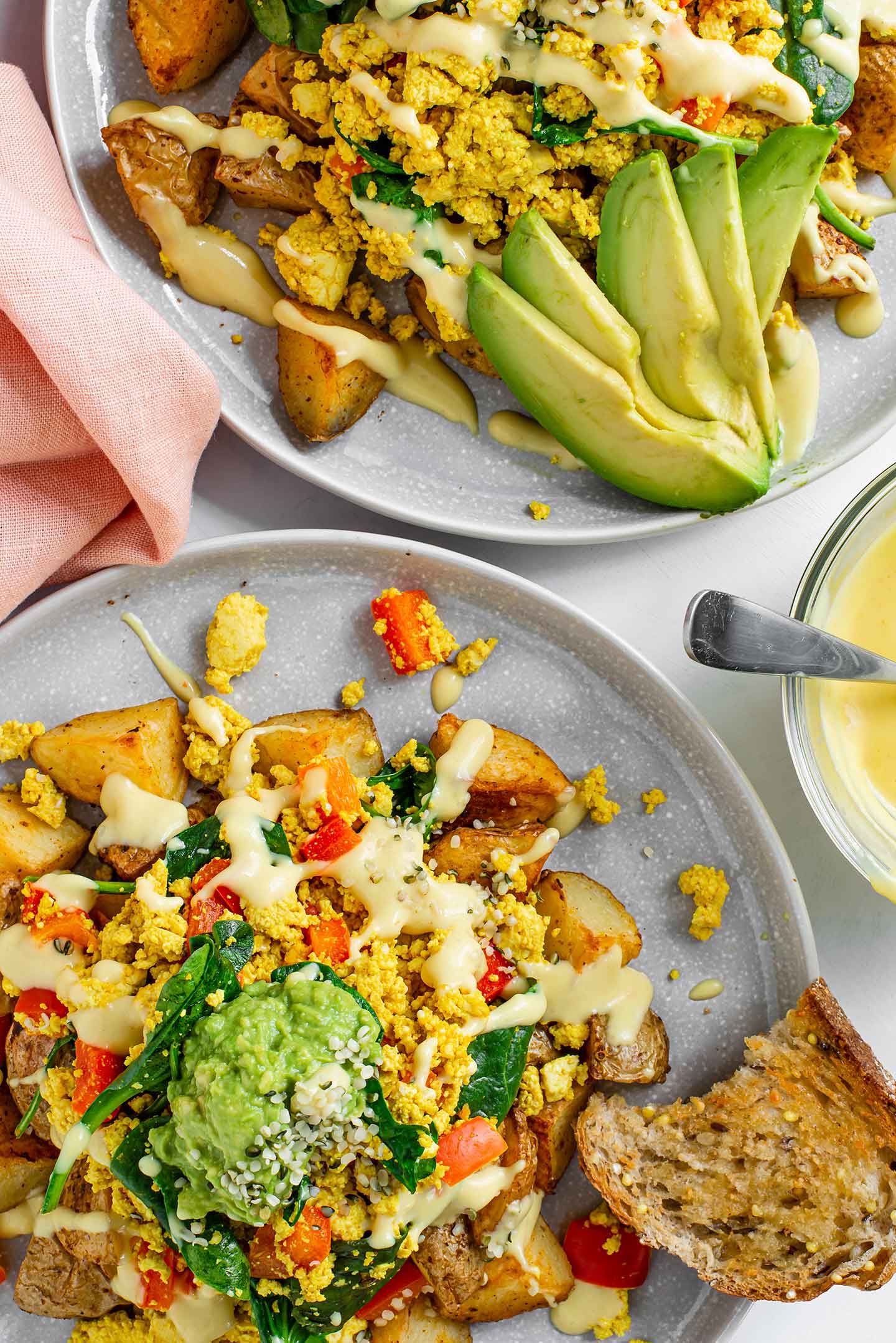 Top down view of ultimate scramble and spuds breakfast bowl with mashed avocado and drizzled queso. Another bowl with sliced avocado fills the top of the image.