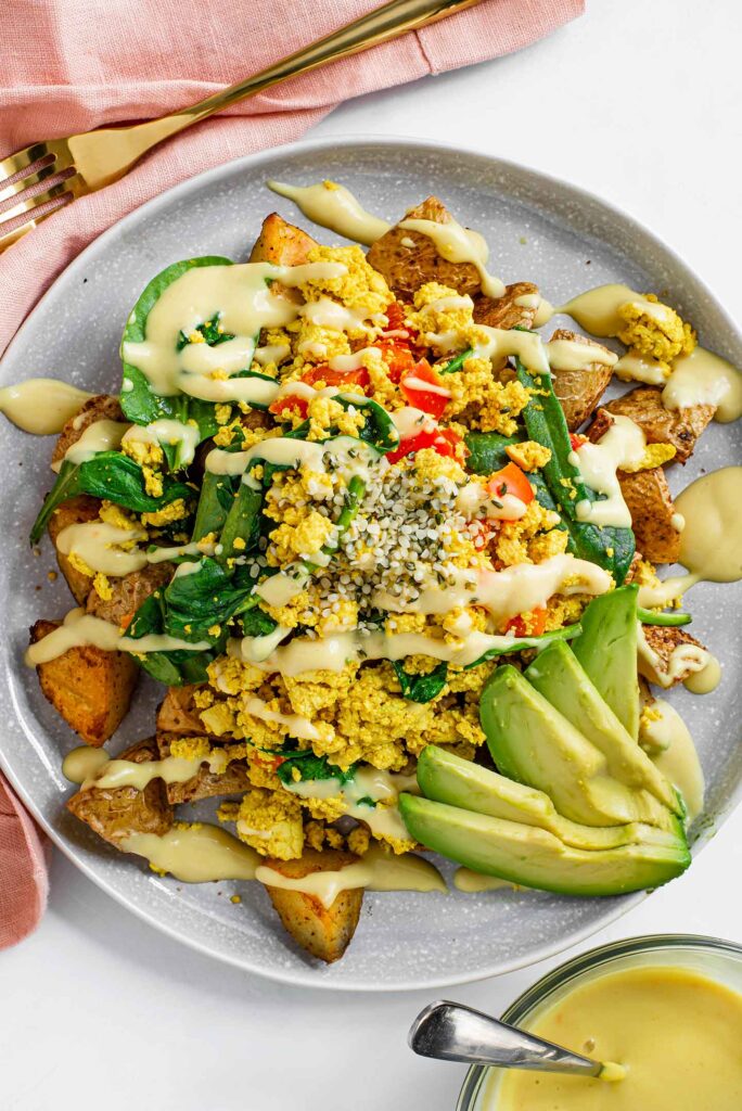 Top down view of ultimate scramble and spuds breakfast bowl with sliced avocado, drizzled queso, and sprinkled hemp hearts.