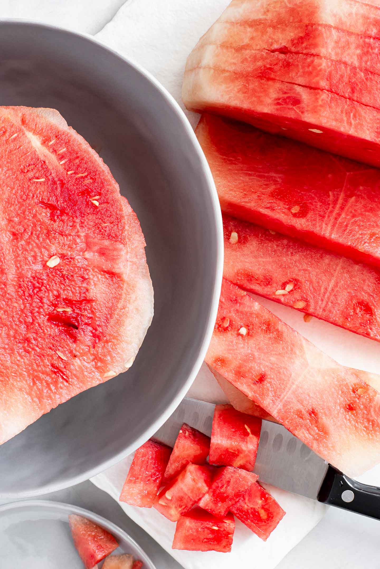 Top down view of a halved watermelon. Half is sliced into rectangular strips. A few pieces are diced into cubes.
