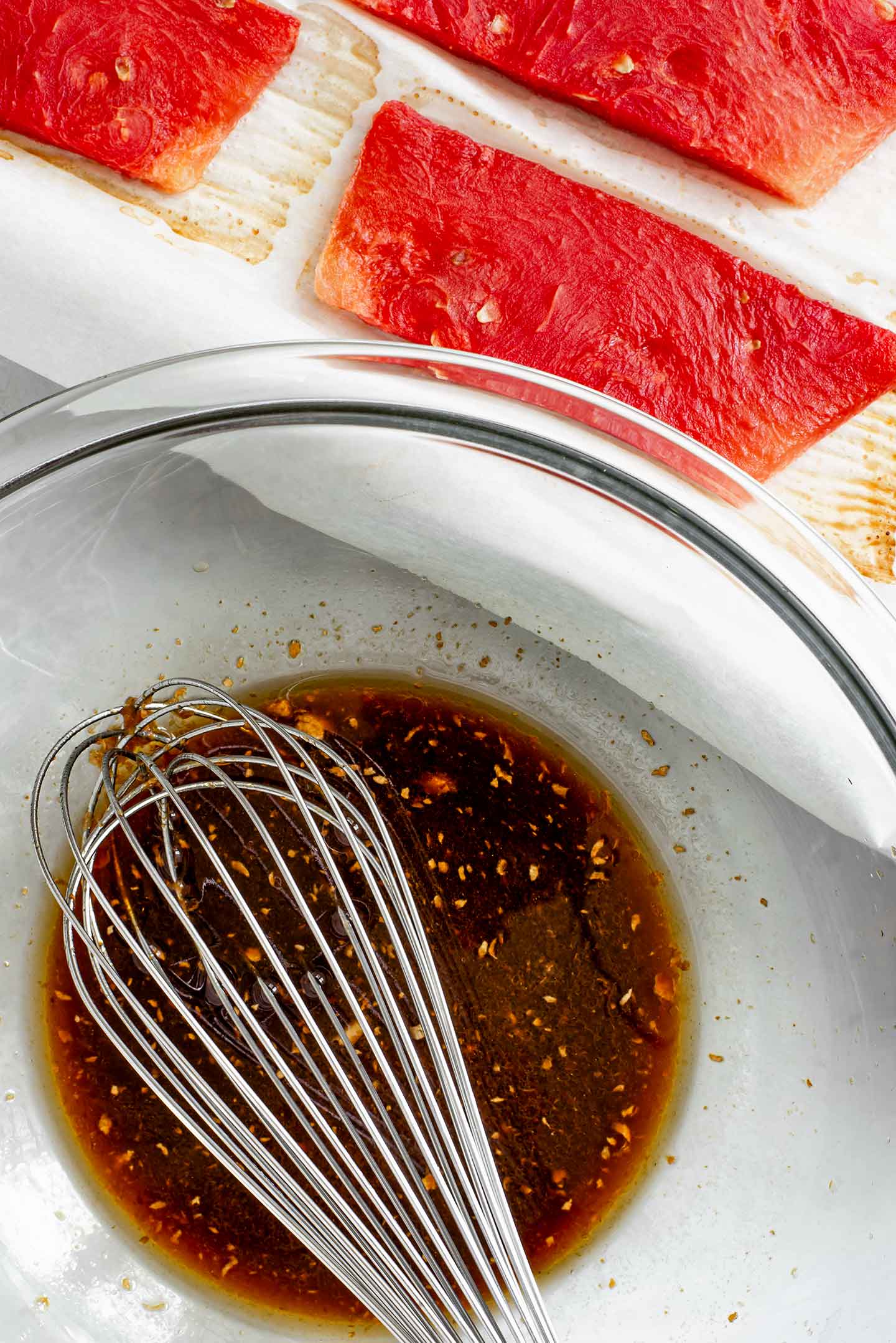 Top down view of the salty, spicy, tangy marinade being whisked in a bowl with the baked steaks on a tray.