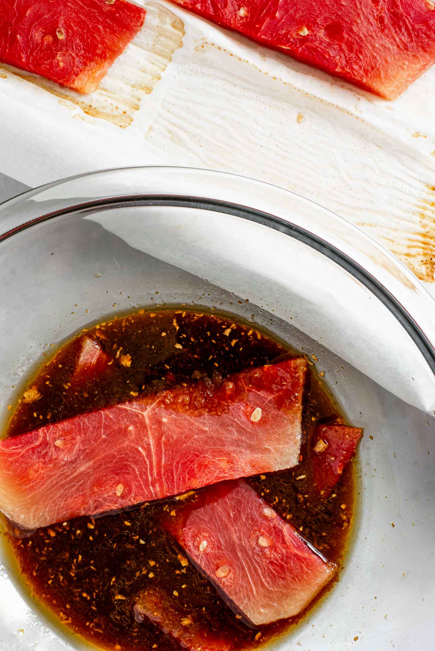 Top down view of baked watermelon steaks being added to a bowl with the dark soy sauce based marinade.
