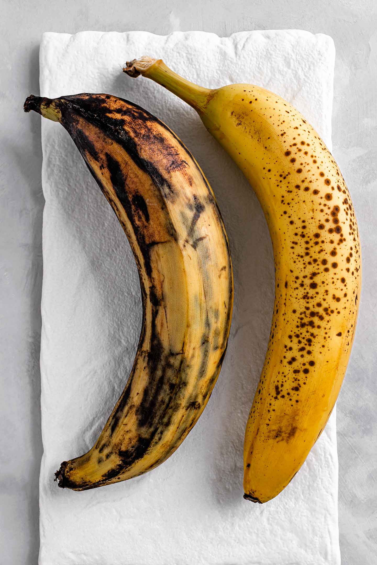 A ripe plantain with black spots next to a ripe banana.