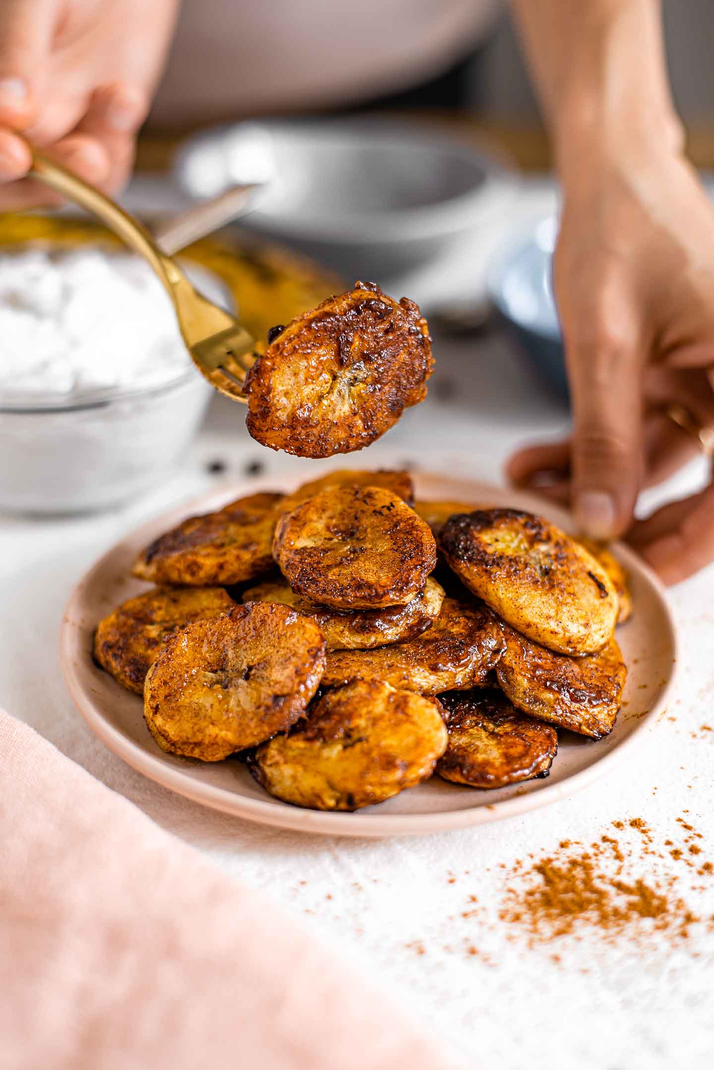 Side view of a plate of caramelized plantains. One golden piece is lifted above the plate on a fork.